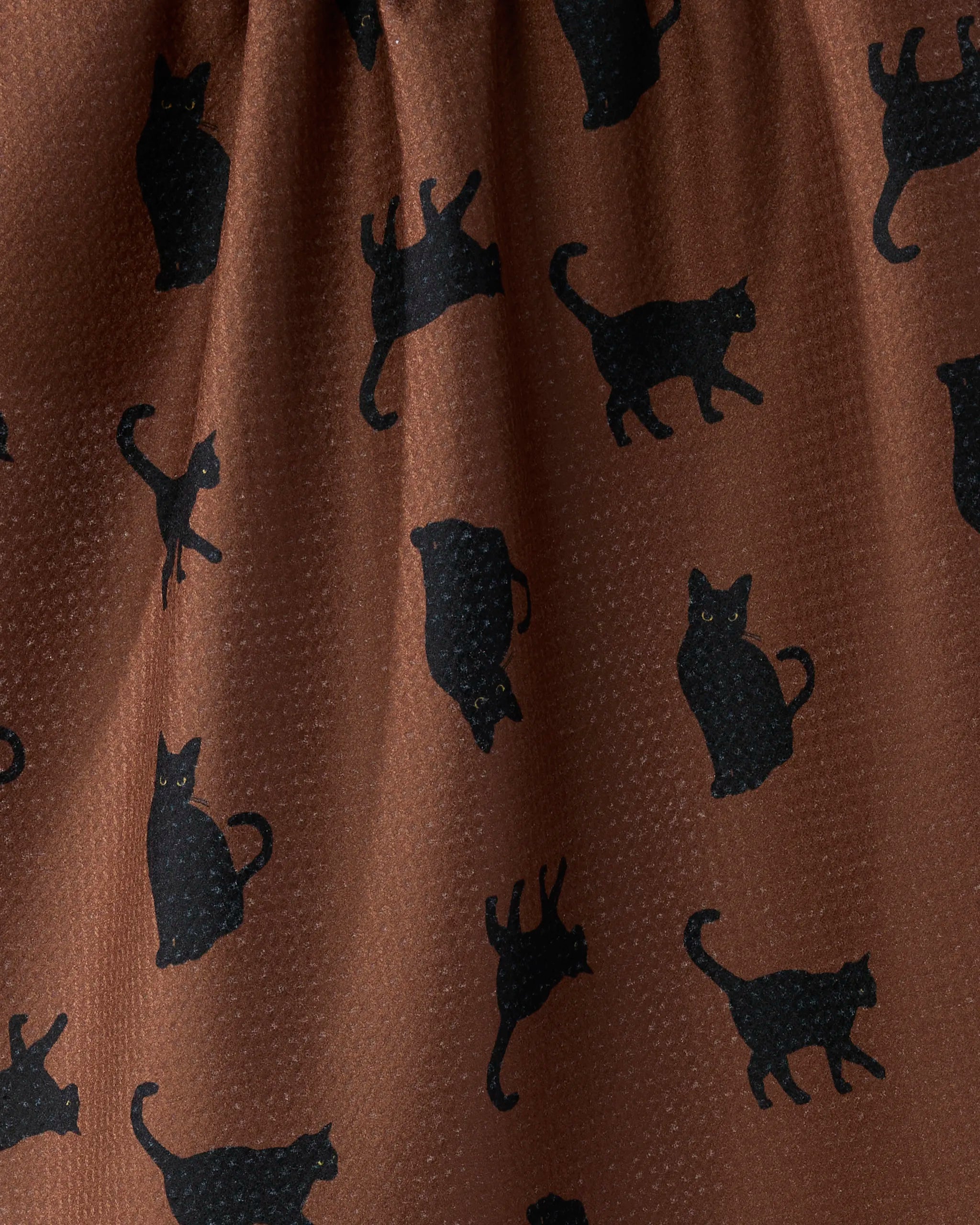 Geometry’s "Witch's Cat" kitchen tea towel features a brown fabric with black cats in various poses. Made from recycled materials, it offers a visible texture and an eco-friendly touch.