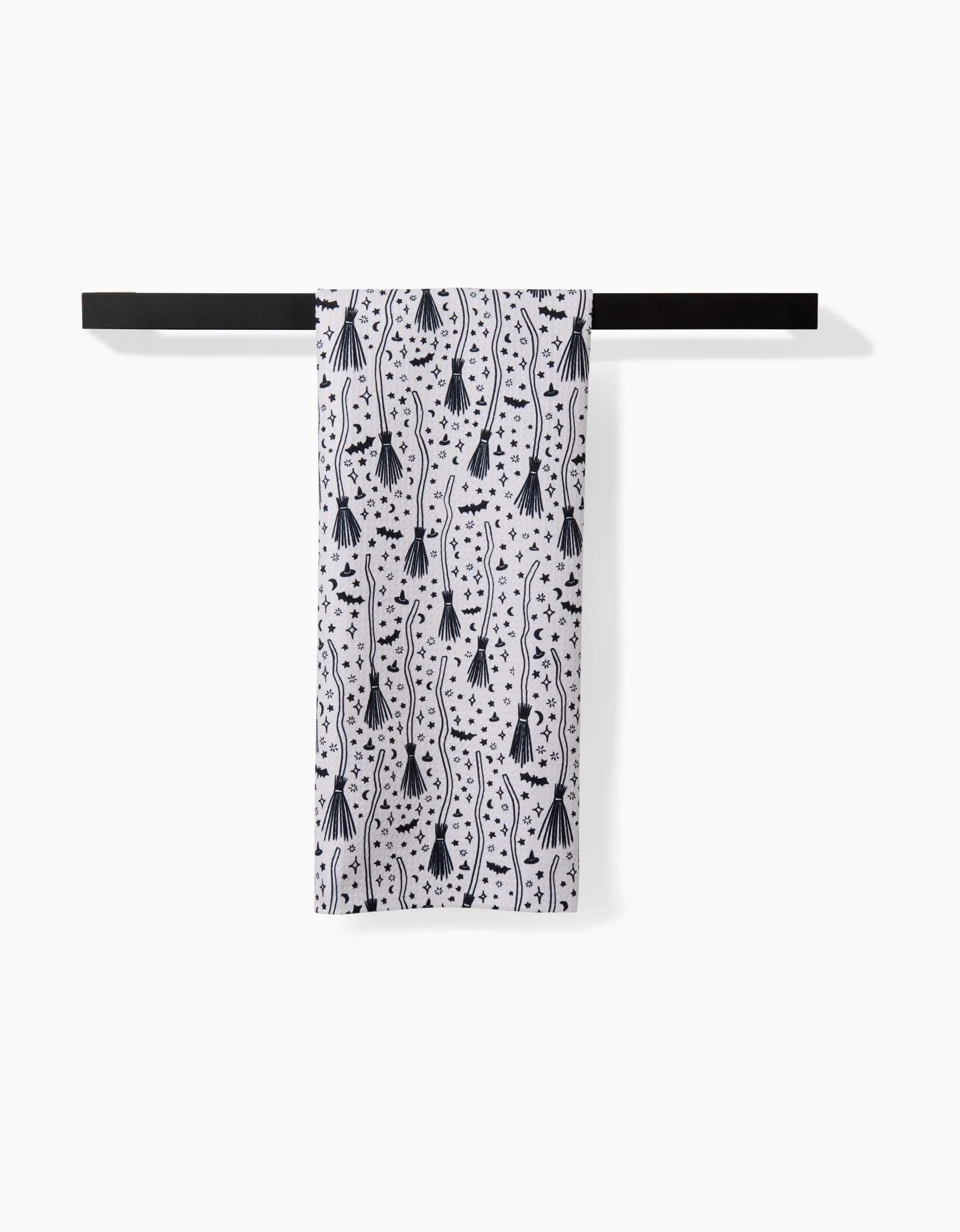 The Kayla Ann Witches Broom tea towel, made from ultra-absorbent recycled materials, features a black abstract pattern of lines, dots, and shapes on white. It hangs neatly on a black bar against a plain white background.