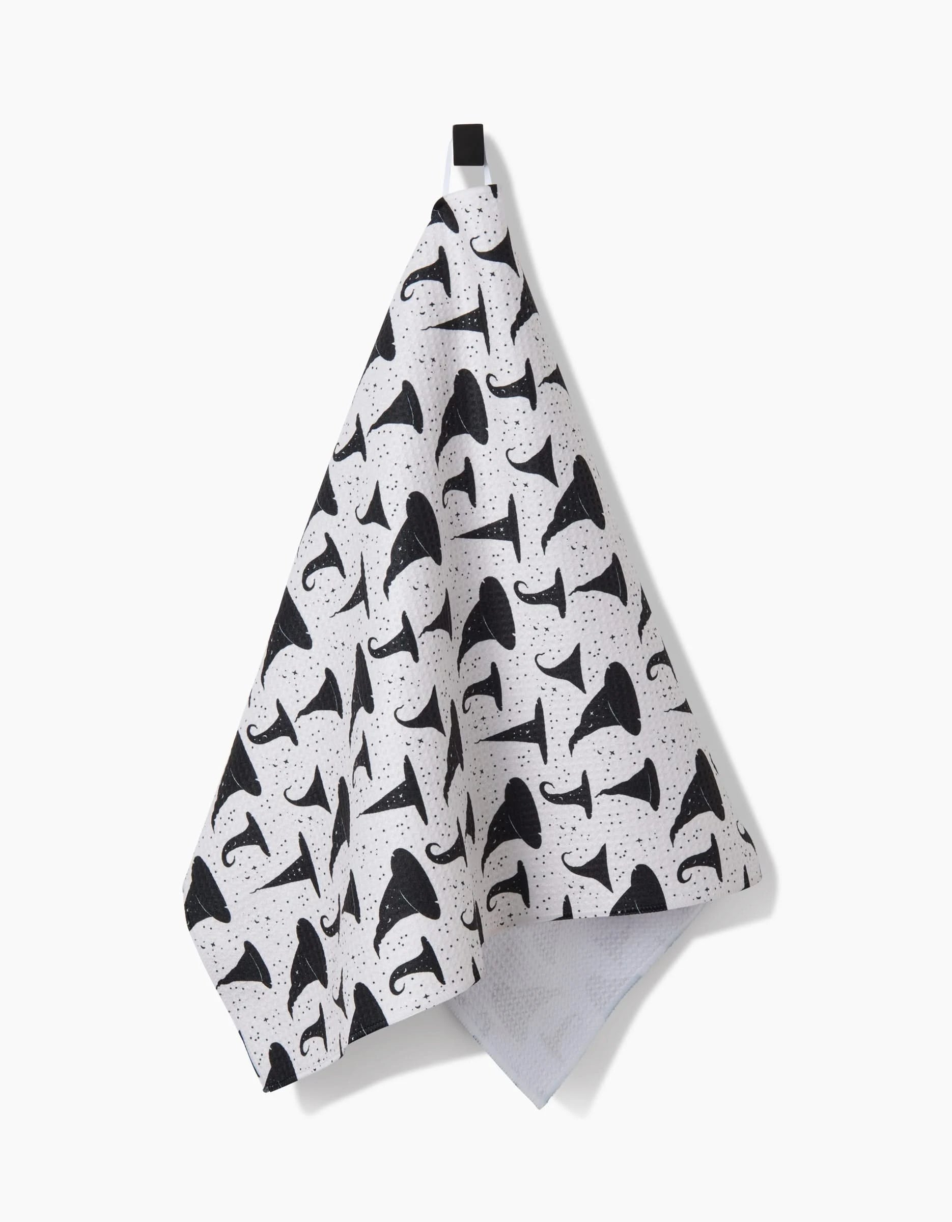 The Witchy Whims kitchen towel by Danelys Sidron features a repeating black mushroom pattern on white, hangs from a black loop, and is crafted from recycled materials.