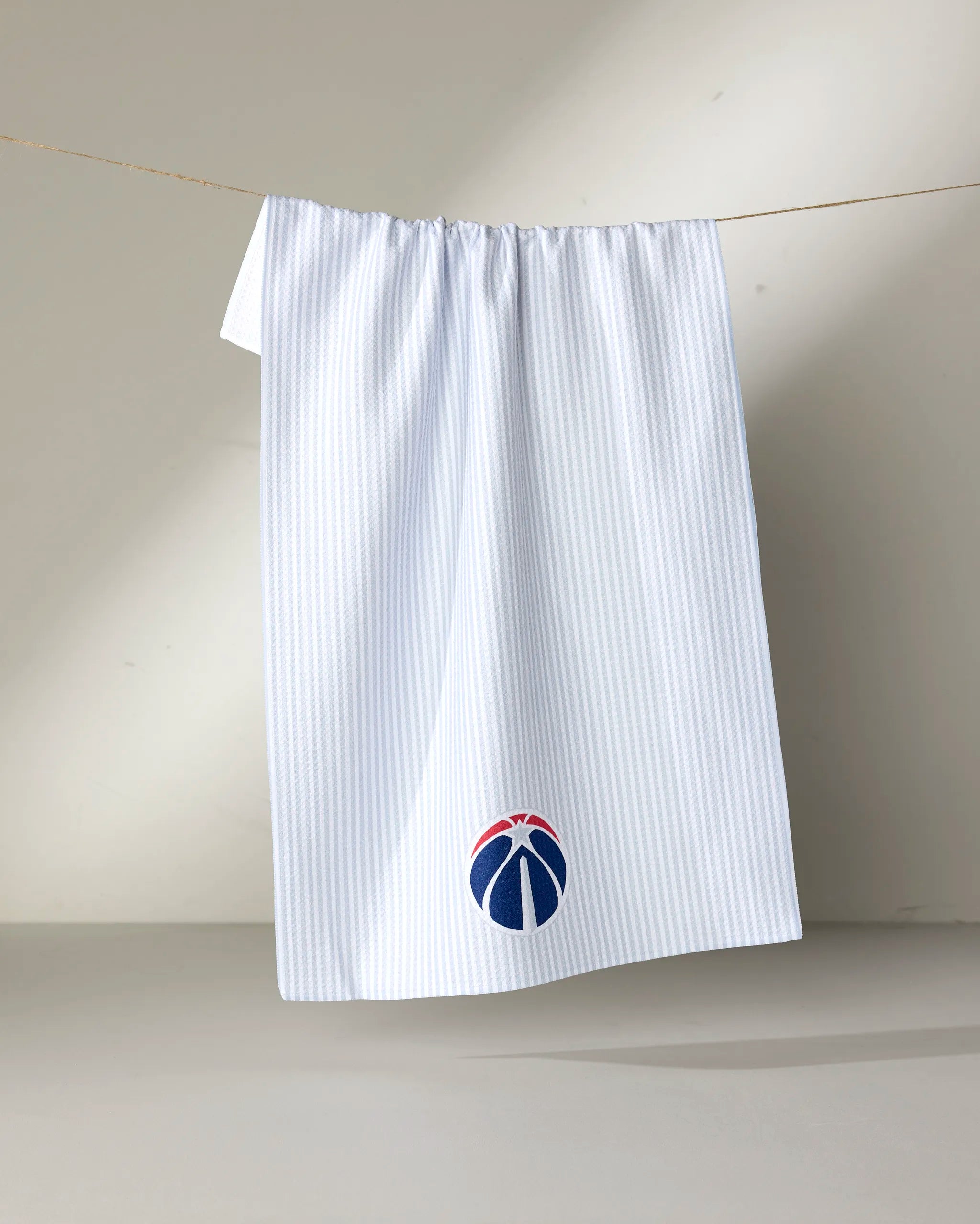 The NBALAB x Geometry "Wizards Classic" is a white, sustainable kitchen towel with subtle blue pinstripes and a stylized basketball logo in the Washington Wizards’ red, white, and blue near the bottom.