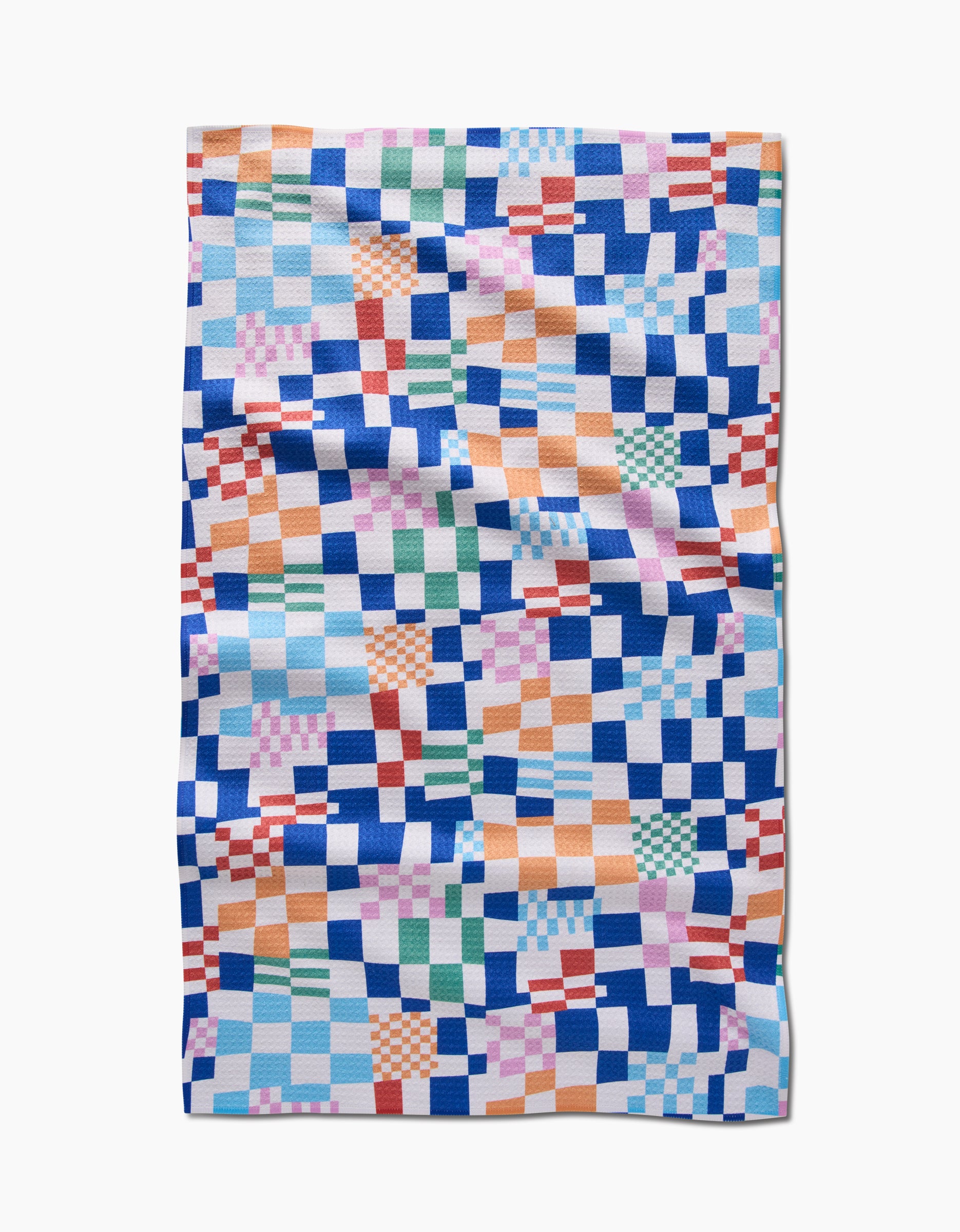 The Wonky Checkers tea towel by Claire Iglesias features a colorful, irregular checkerboard in blue, orange, green, pink, and white squares. Made from recycled materials, it’s quilted and shown flat with visible folds and creases.