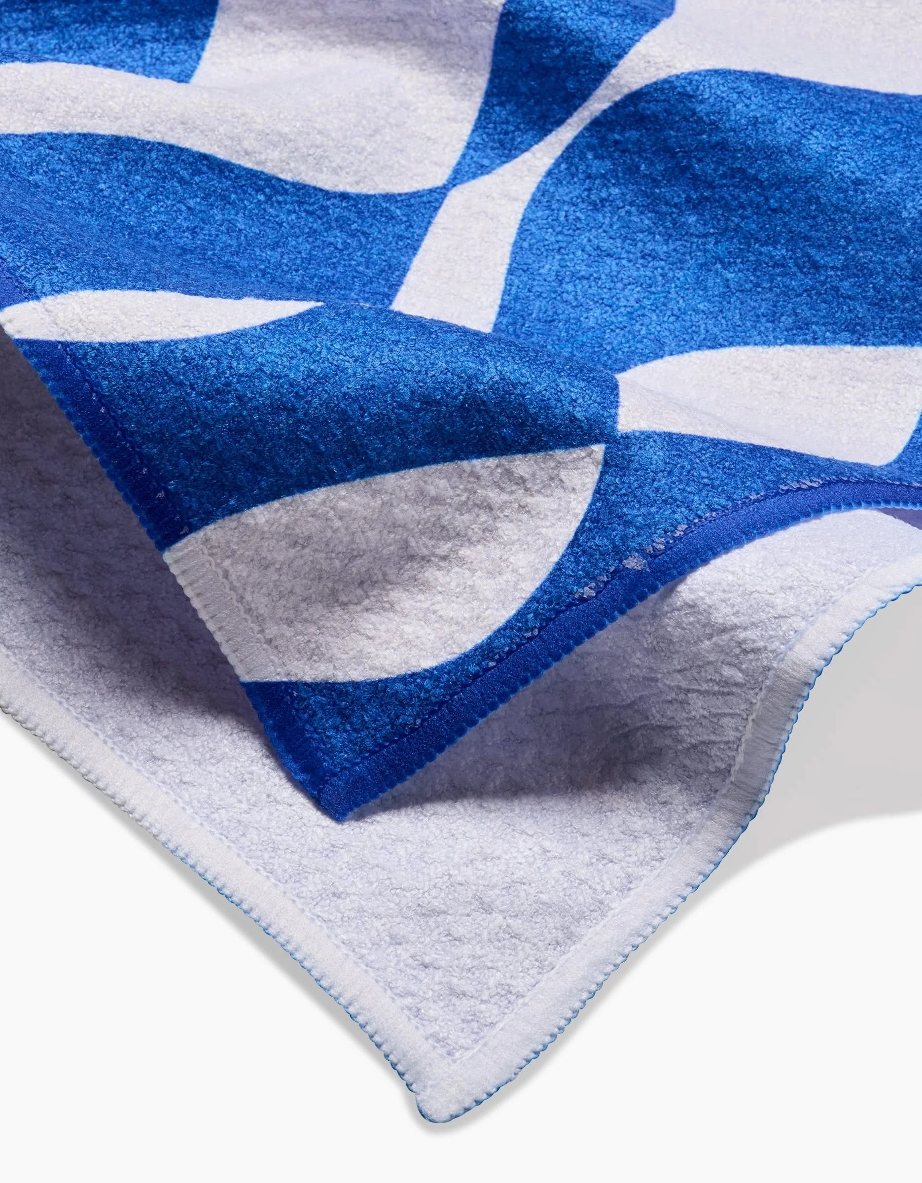 A close-up of the Wonky Lines tea towel by Claire Iglesias, featuring soft blue and white curved abstract patterns, stitched edges, and crafted from recycled materials, shown on a white surface.