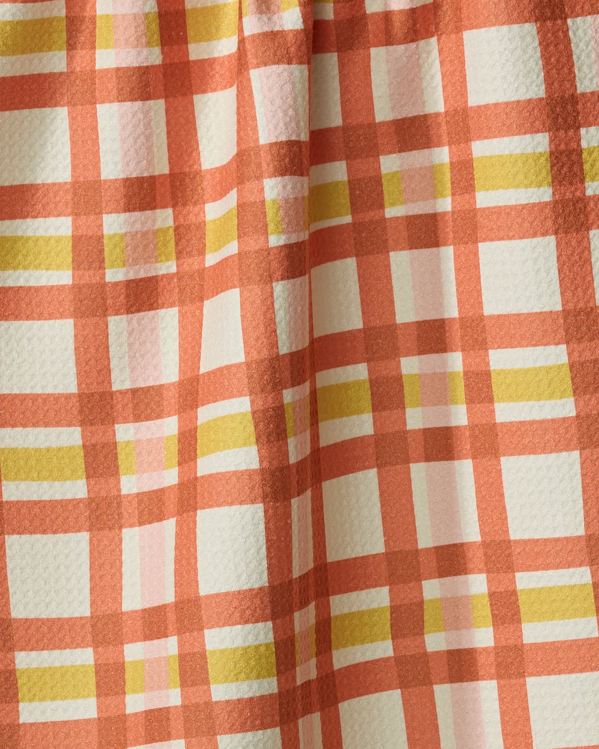 A close-up of the Wonky Plaid kitchen towel by Kelsey Weigl shows its absorbent, textured fabric with a coral, yellow, and white plaid pattern. Soft folds and shadows add depth to the checked design.