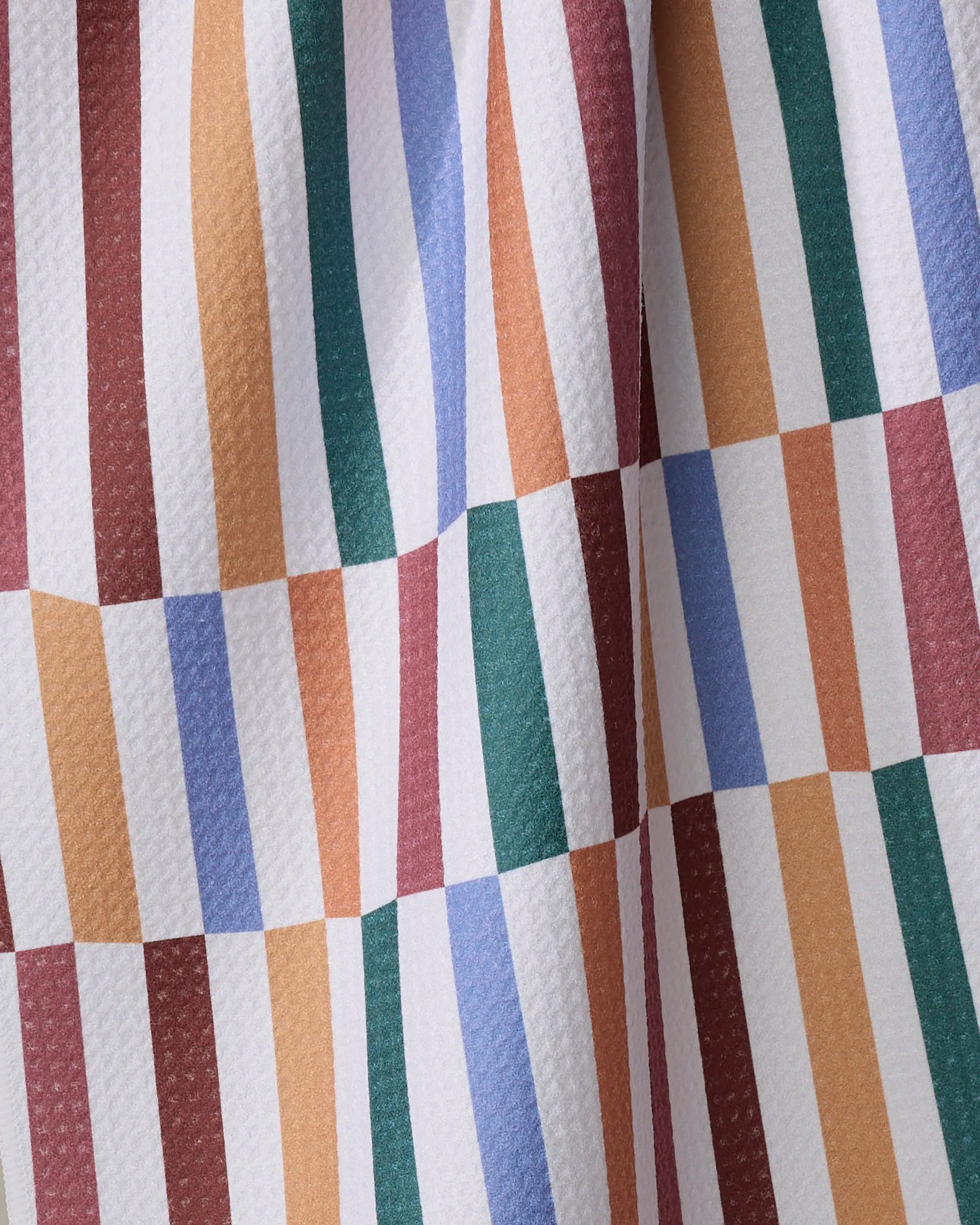 The Wonky Stripes tea towel by Claire Iglesias features green, brown, red, orange, and blue stripes on textured white—creating a geometric, checkered look. Made from recycled materials for an eco-friendly touch.