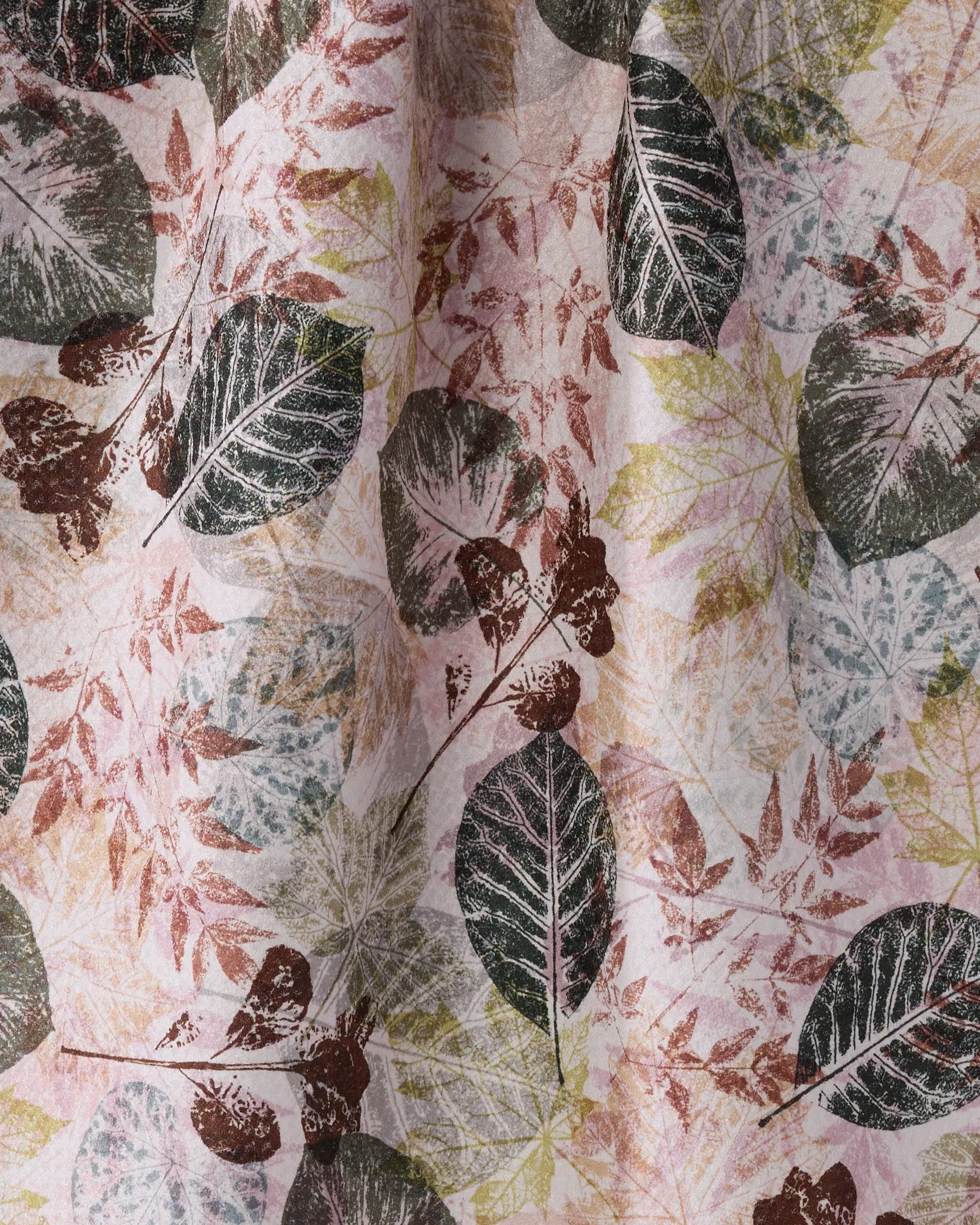 A close-up of Geometry's Woodland Press tea towel reveals ultra-absorbent fabric adorned with layered green, brown, and pink leaf patterns on a light background for a textured effect.