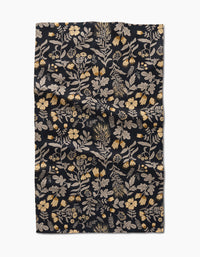 The Danelys Sidron Woodland Wildflowers tea towel is a dark rectangular cloth with yellow and cream floral botanical patterns, made from recycled materials. The slightly wrinkled fabric is shown flat on a white background.