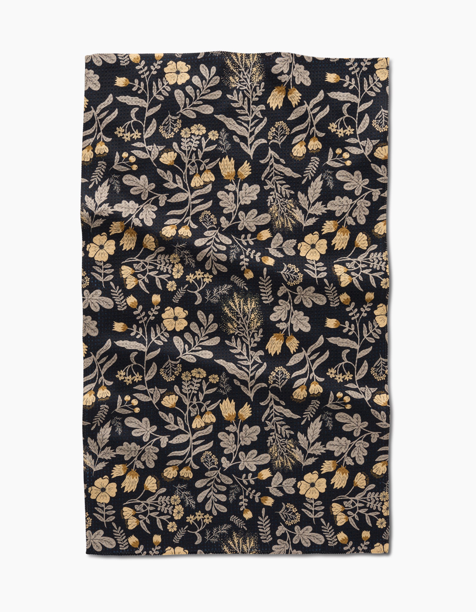 The Danelys Sidron Woodland Wildflowers tea towel is a dark rectangular cloth with yellow and cream floral botanical patterns, made from recycled materials. The slightly wrinkled fabric is shown flat on a white background.