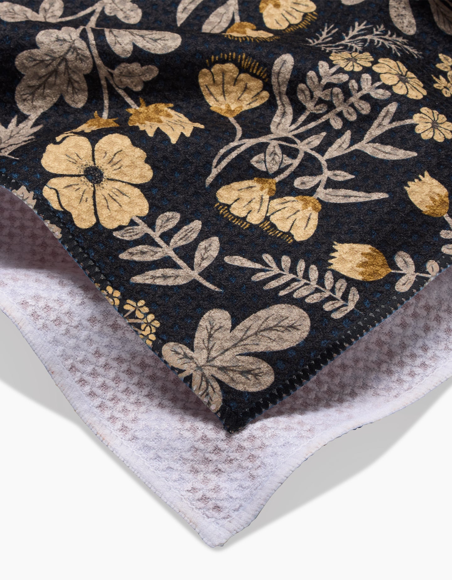 A close-up of Danelys Sidrons Woodland Wildflowers: a dark fabric with gold and beige floral patterns, layered over an ultra-absorbent white waffle-knit tea towel.