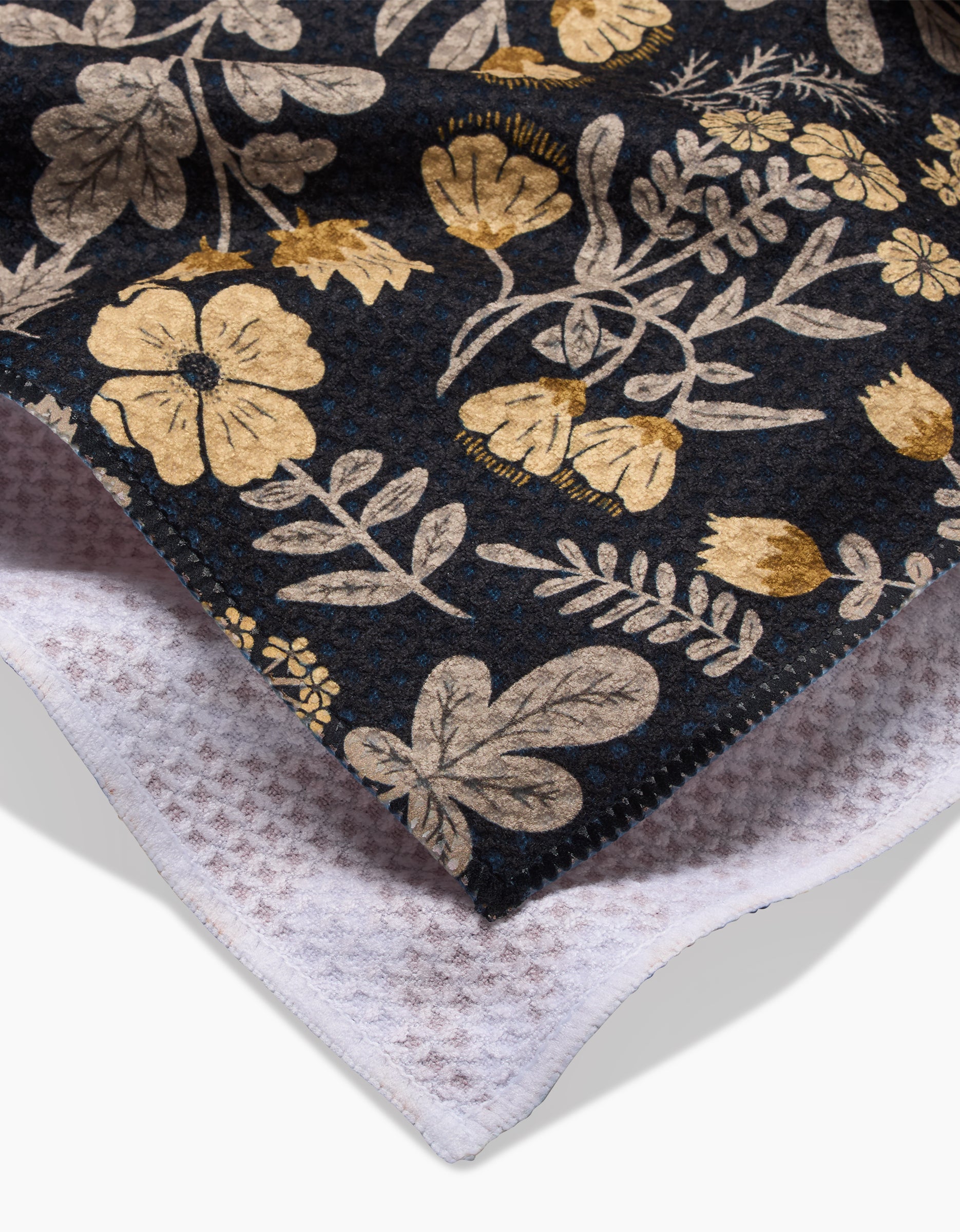 A close-up of Danelys Sidrons Woodland Wildflowers: a dark fabric with gold and beige floral patterns, layered over an ultra-absorbent white waffle-knit tea towel.