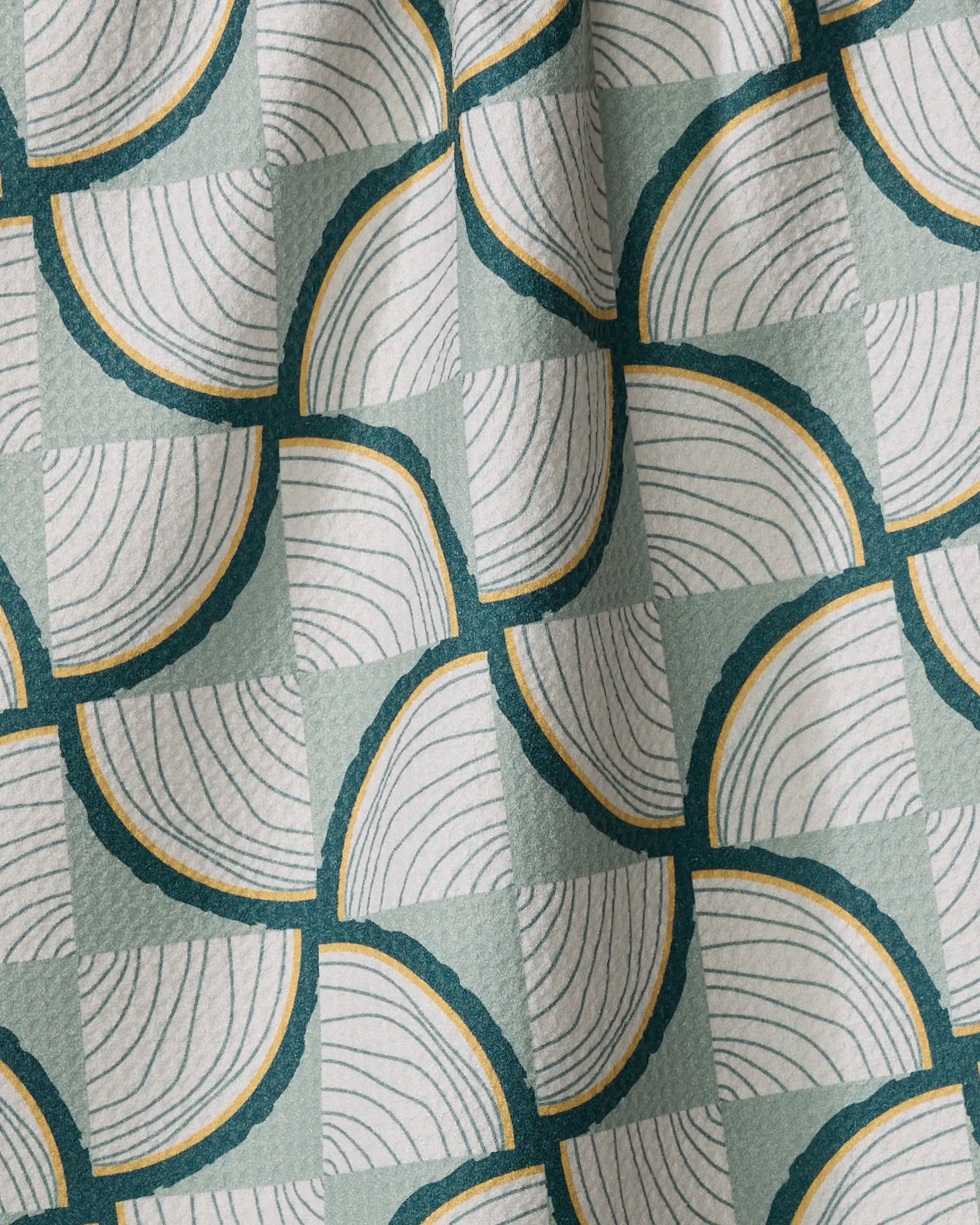 Close-up of the Twig + Spark Woodpile recycled kitchen towel, showing overlapping semi-circles and curved lines in dark green, yellow, and white on a light green checkered background with a slightly wrinkled texture.