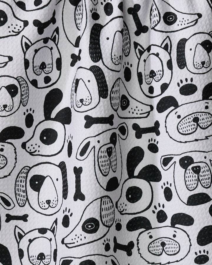 The "Woofin Around" kitchen towel by Jessica Swift features playful black and white cartoon dog faces, bones, and paw prints. Eco-friendly and charming, its whimsical design brightens your daily routine.