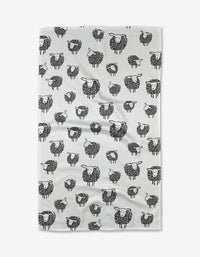 The Wooly Sheep kitchen towel by Kris Ruff is white, made from recycled material, and features an even pattern of black and white cartoon sheep in various poses.