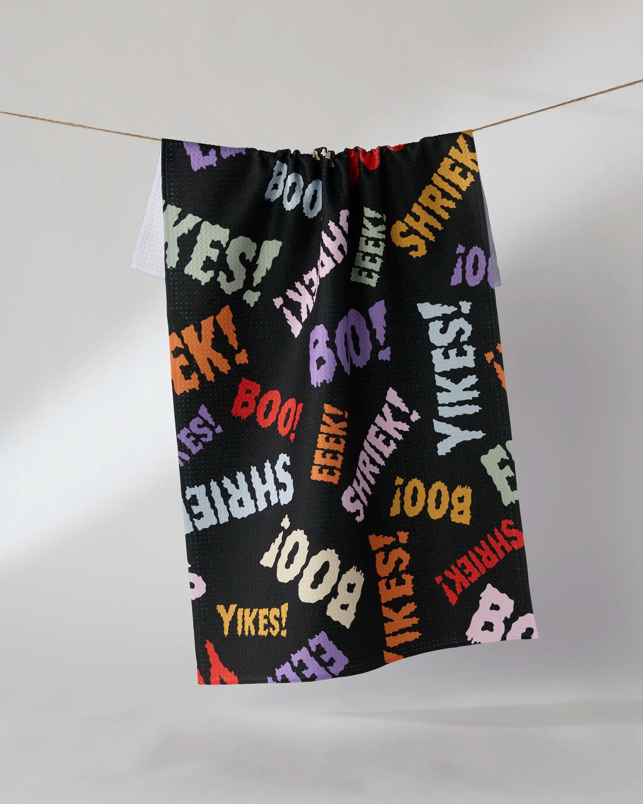 The Geometry Word Fright kitchen towel, made from recycled materials, features a black background with colorful "Yikes!", "Boo!", "Eek!", and "Shriek!" words in white, purple, orange, red, and green fonts.
