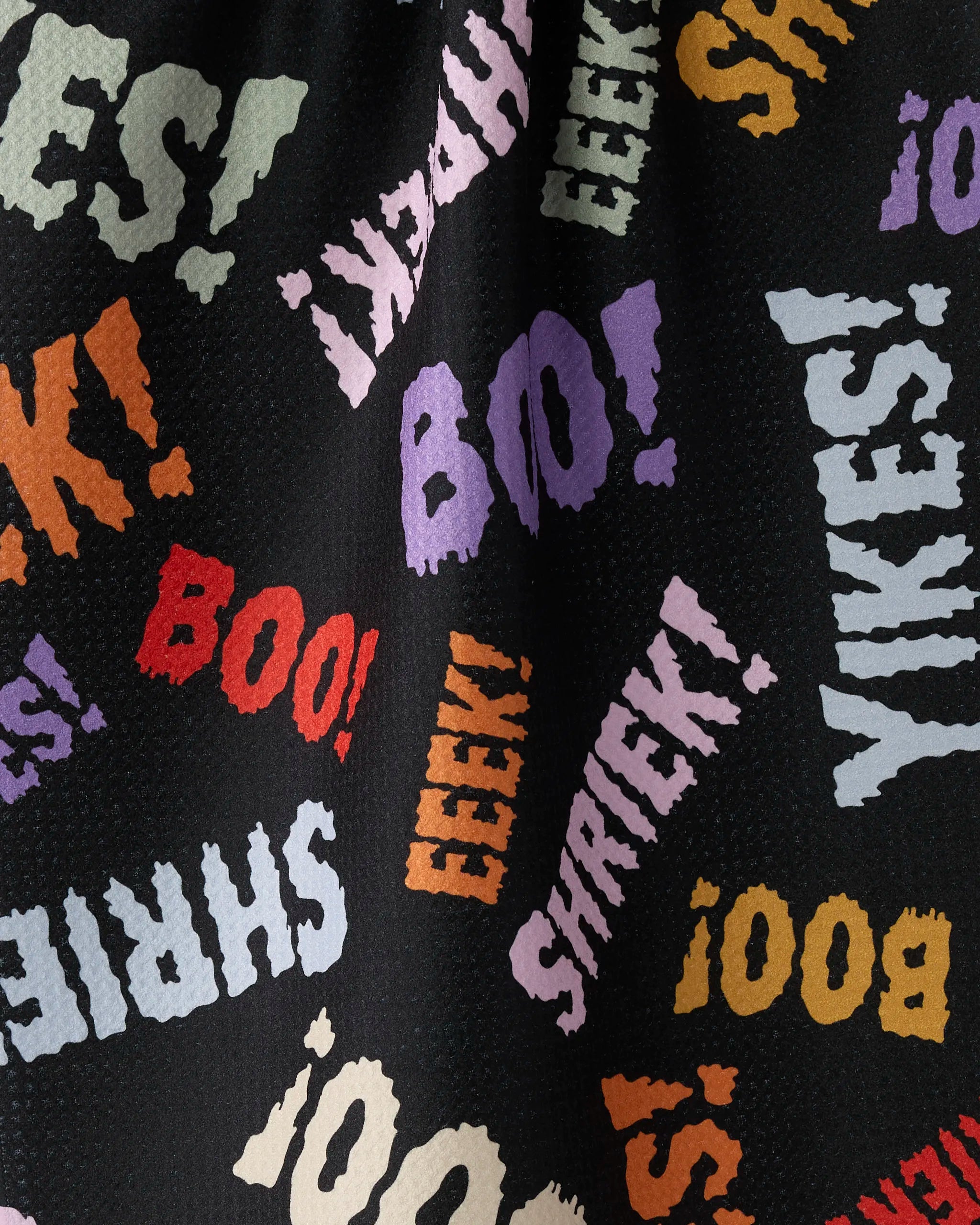Geometry’s Word Fright features black fabric with vibrant words—BOO!, YIKES!, SHRIEK!, EEEK!—in playful sizes for a spooky Halloween vibe, making it perfect for a festive tea towel crafted from recycled materials.