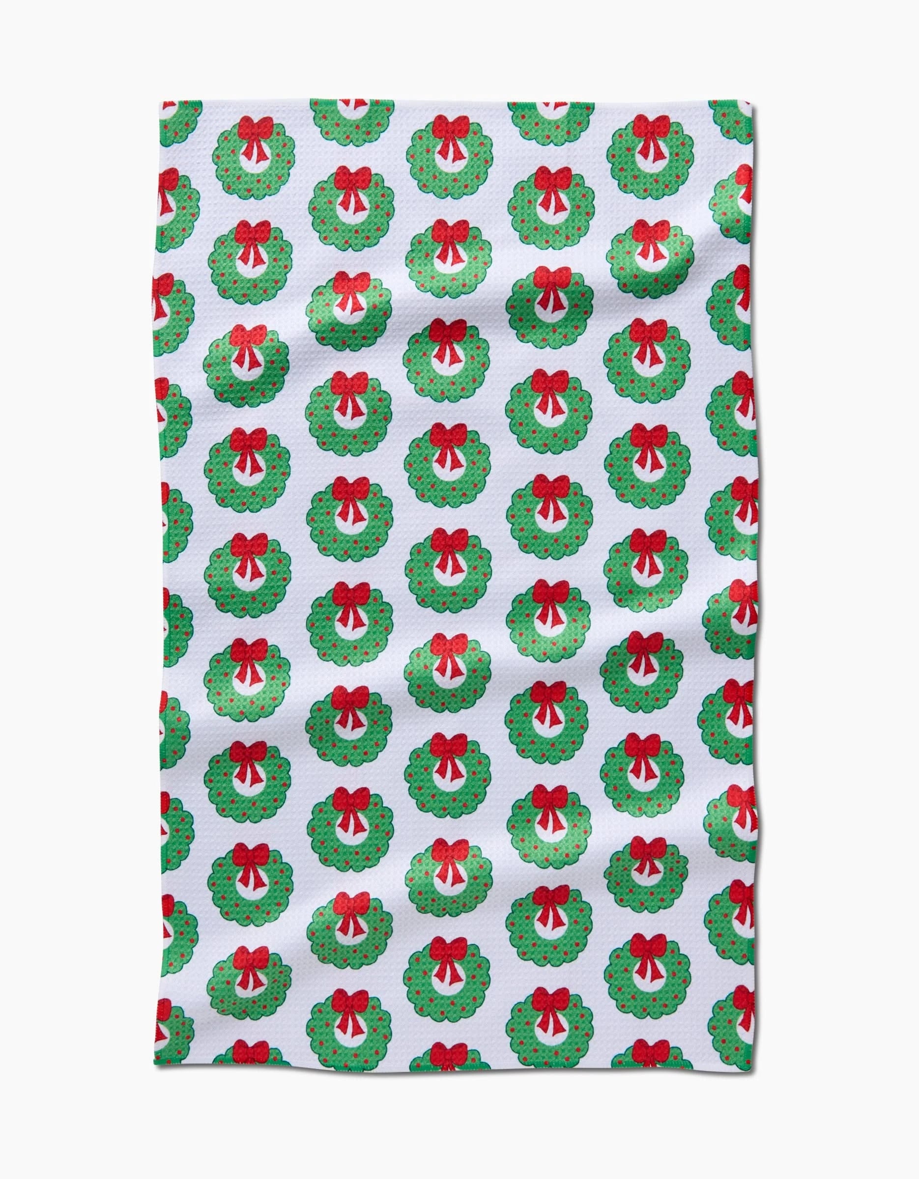 The Mindfulnice Wreath Wishes tea towel features a pattern of green Christmas wreaths with red bows and berries. Made from recycled materials, this ultra-absorbent kitchen towel displays evenly spaced wreaths in neat rows.