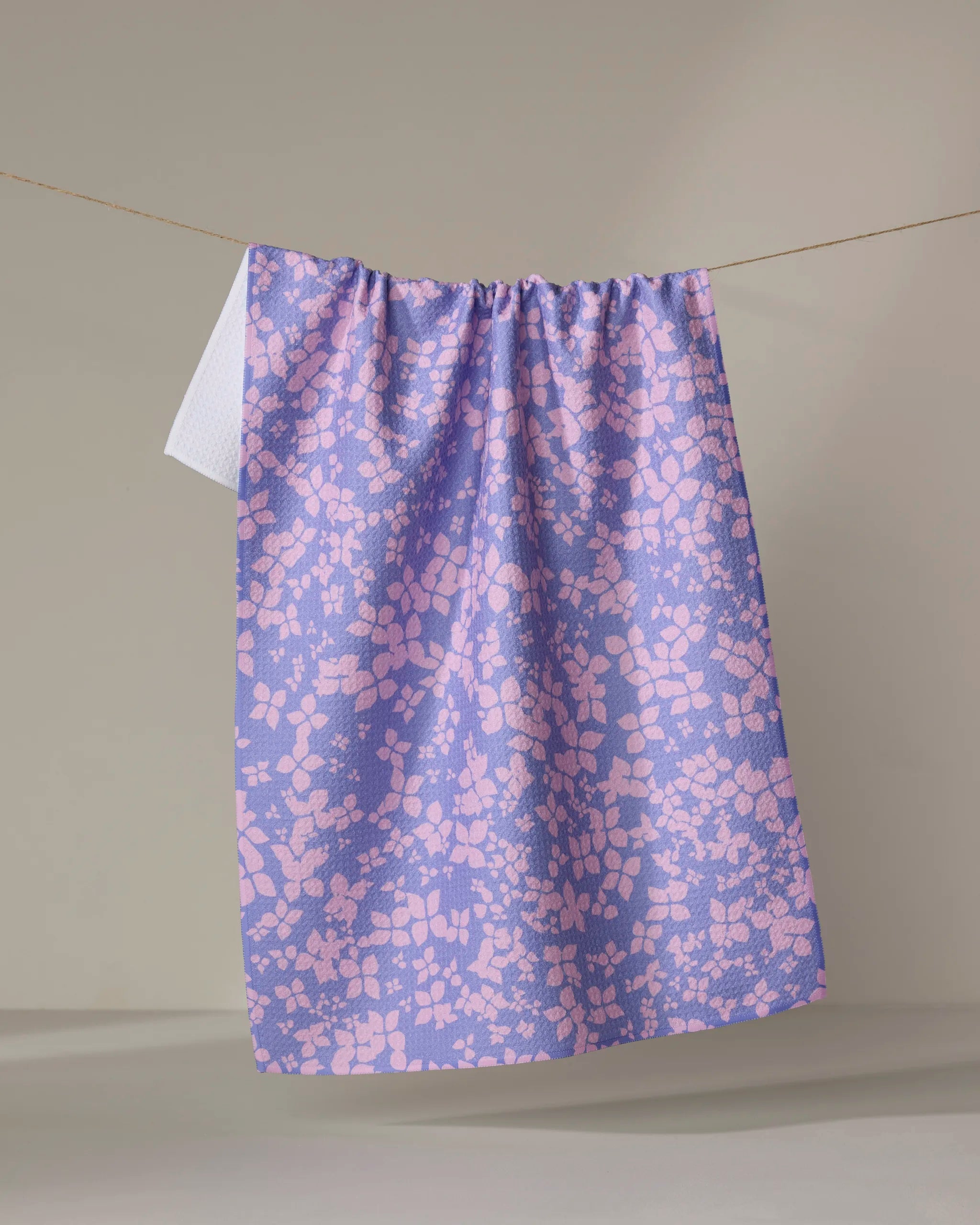 The Sareka Unique "You Give Me Butterflies" tea towel, featuring a purple and pink pattern, hangs neatly on a clothesline against a plain, light-colored background.