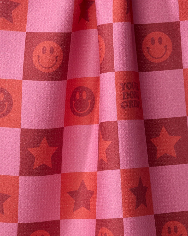 The "You’re Doing Great" tea towel by Quotes by Christie features pink and red checkered squares with smiley faces, stars, and a motivational message, crafted from ultra-absorbent recycled materials.