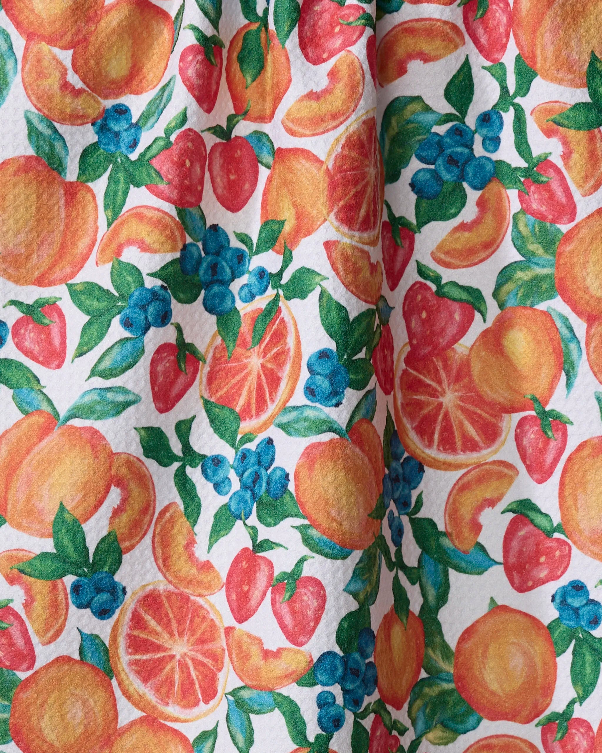 The Zesty Life tea towel by Aubrey Fairchild features a vibrant pattern of oranges, strawberries, blueberries, peaches, and green leaves on white—making it a colorful and practical kitchen accessory.