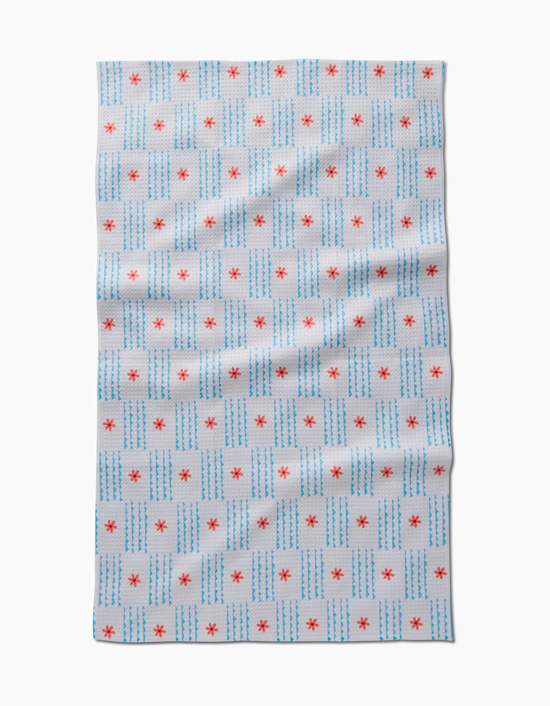 The Ziggy Floral by Elizabeth Edwards is a white tea towel with blue dashed grid lines and small red stars at some intersections, made from recycled materials. It’s shown flat with slight wrinkles.