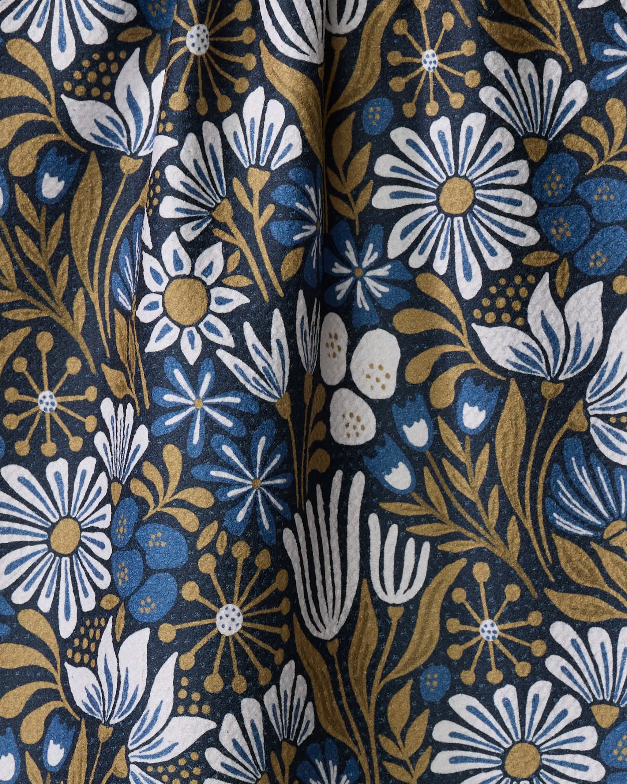 Zillia by Amy MacCready is an eco-friendly fabric crafted from recycled materials, featuring a floral pattern of white and blue flowers with gold stems and leaves on a dark background for a vibrant, detailed look.