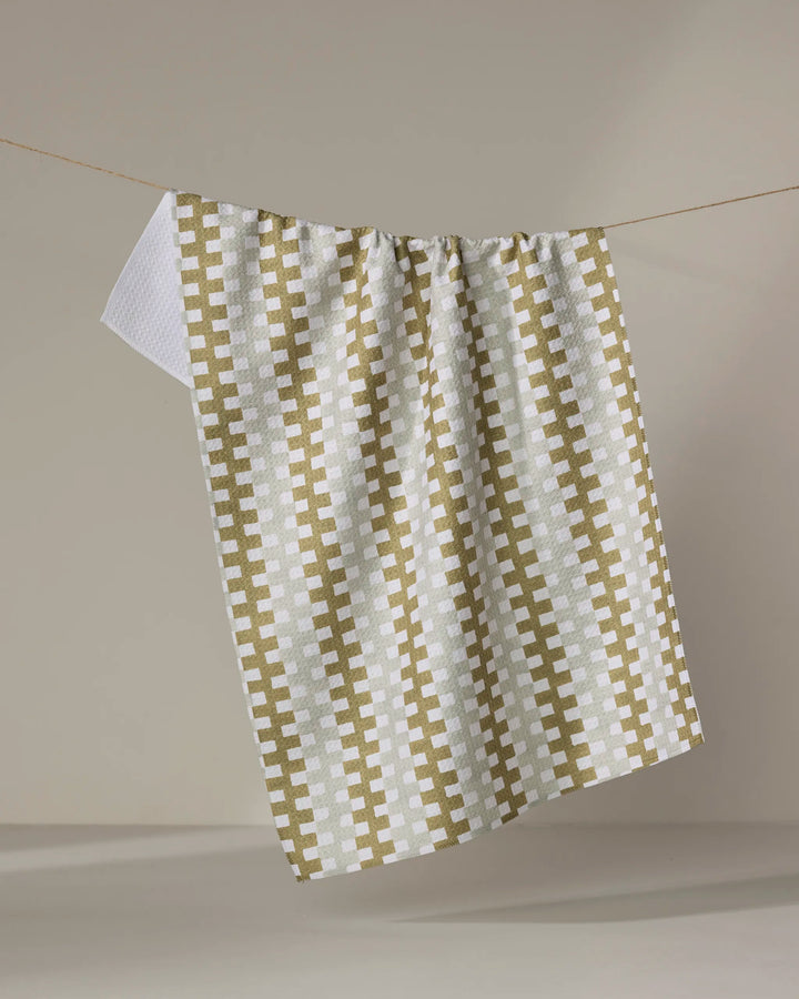 The Zippy tea towel by Studio Jeannot, featuring a green and white checkered design and made from quick-drying recycled materials, hangs on a string against a plain beige background.