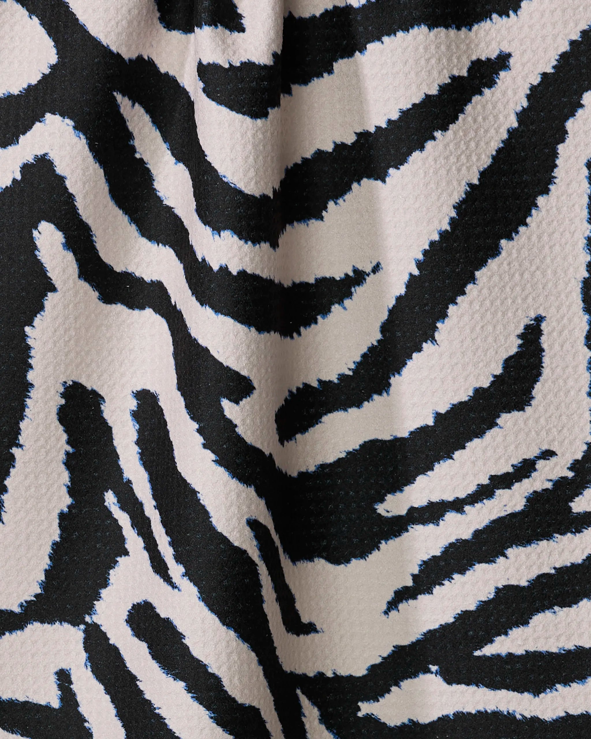 Close-up of Geometry's Zira Black tea towel featuring a black and white zebra print, made from recycled materials with a textured, ultra-absorbent fabric and soft folds that form a wavy pattern.