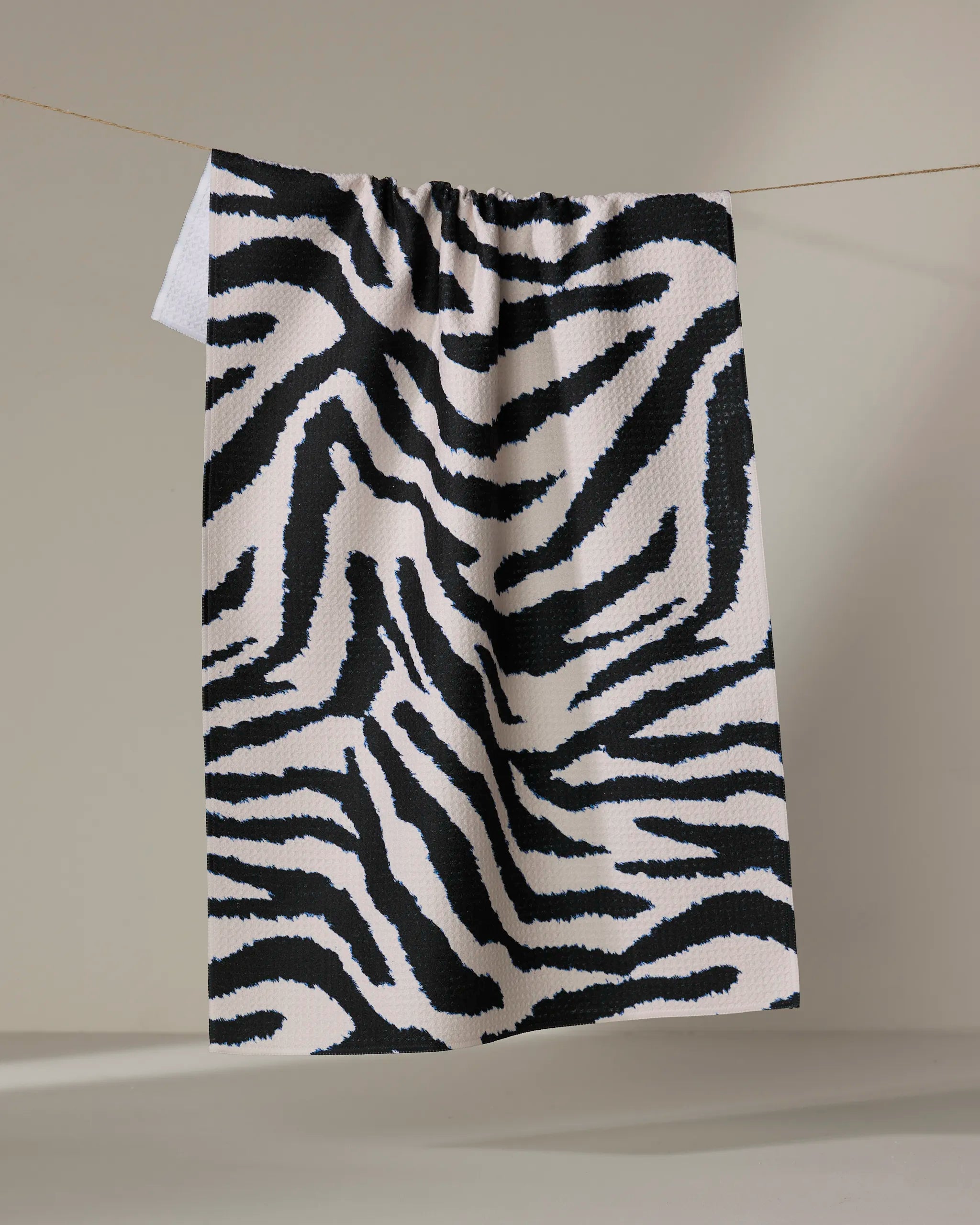 The Geometry Zira Black tea towel, featuring bold black zebra stripes and made from recycled materials, hangs from a string against a neutral background.