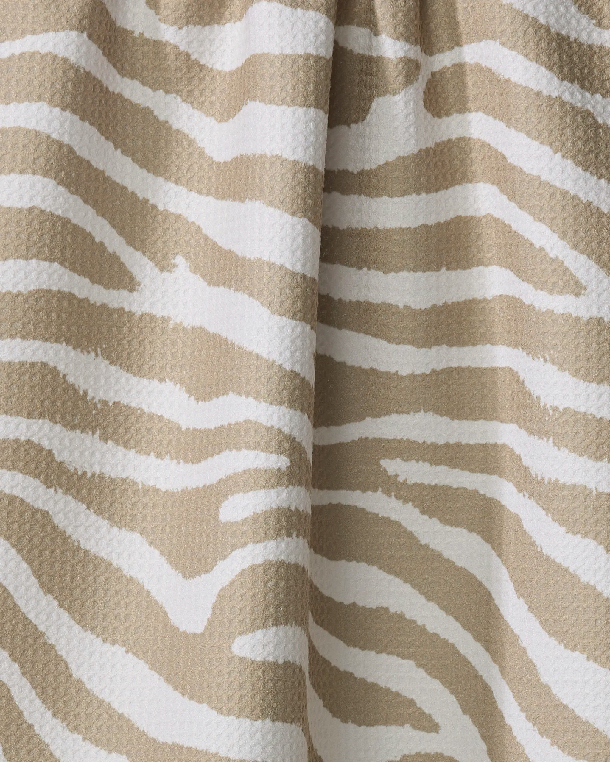 Close-up of Zira Tan by Geometry, an eco-friendly kitchen towel with beige and white zebra-inspired stripes and a textured, slightly wavy surface.