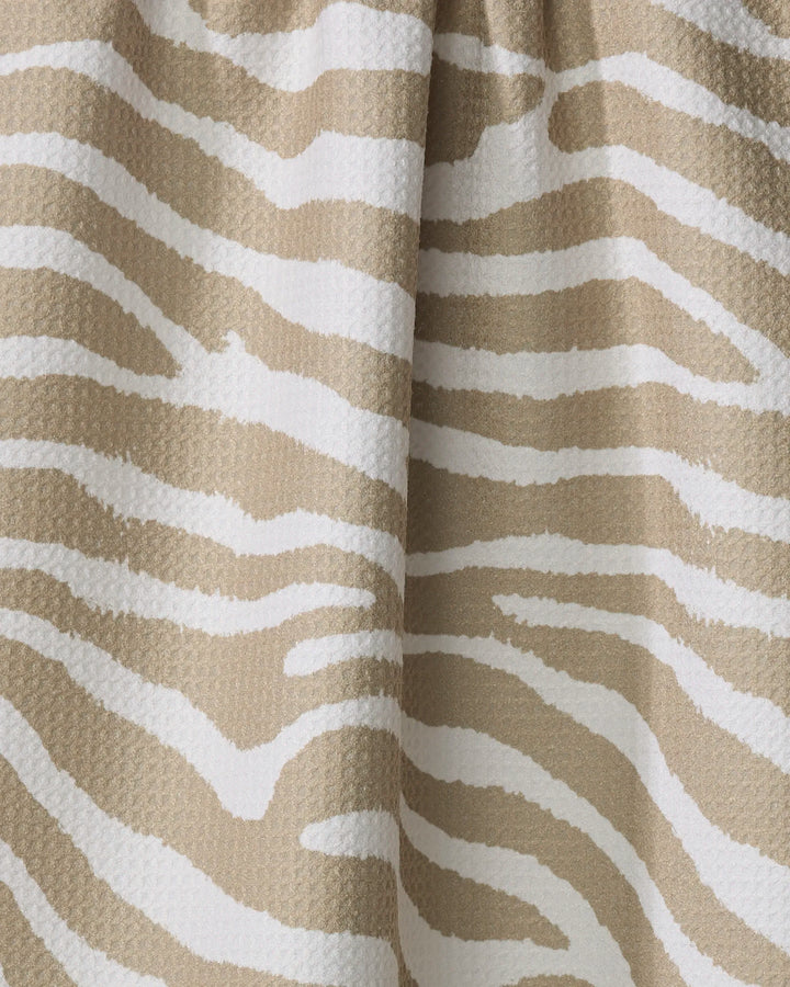 Close-up of Zira Tan by Geometry, an eco-friendly kitchen towel with beige and white zebra-inspired stripes and a textured, slightly wavy surface.