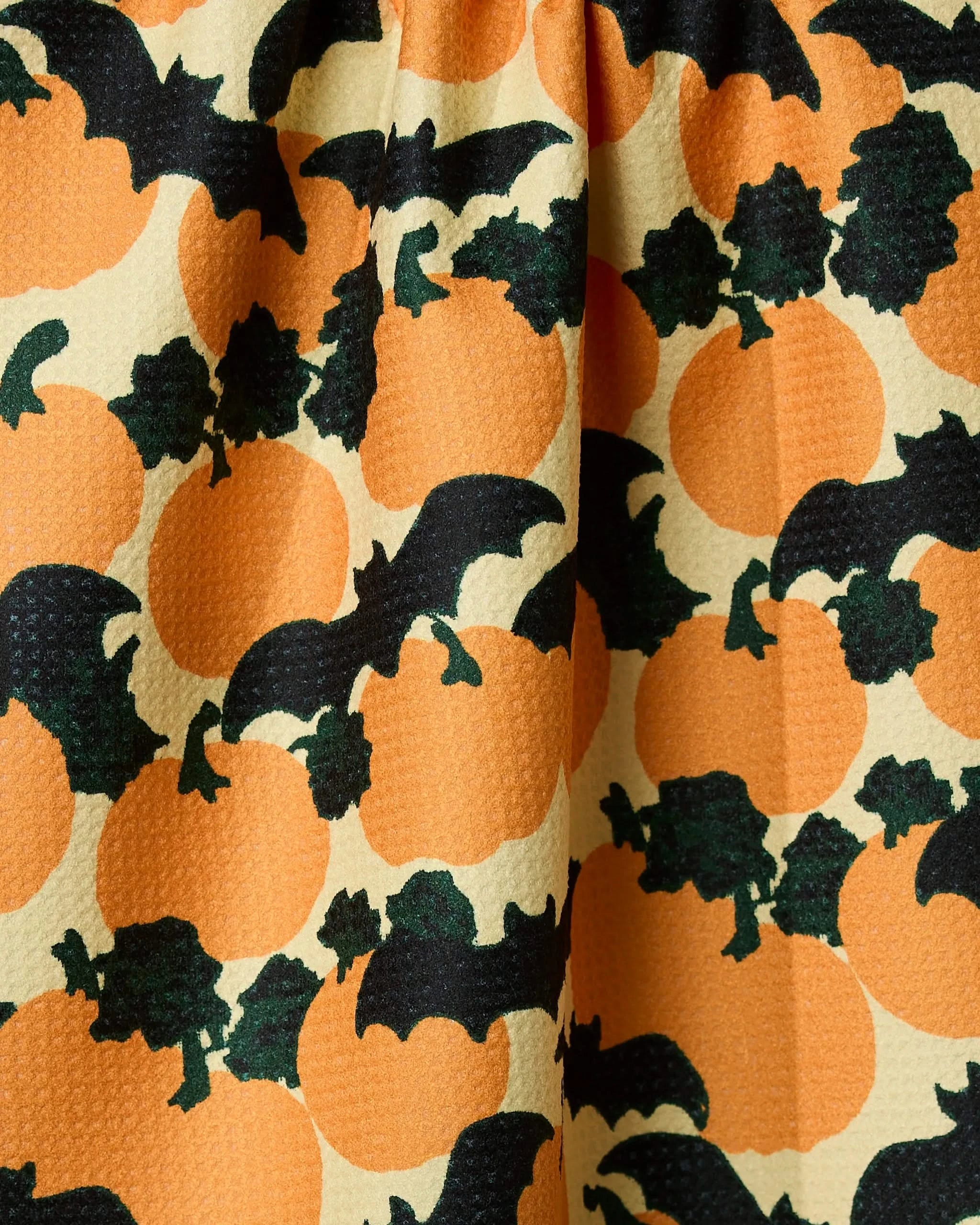 The Geometry Bat Flight tea towel is made from recycled materials and features orange pumpkins, black bats, and dark green leaves on a light background—perfect for Halloween.