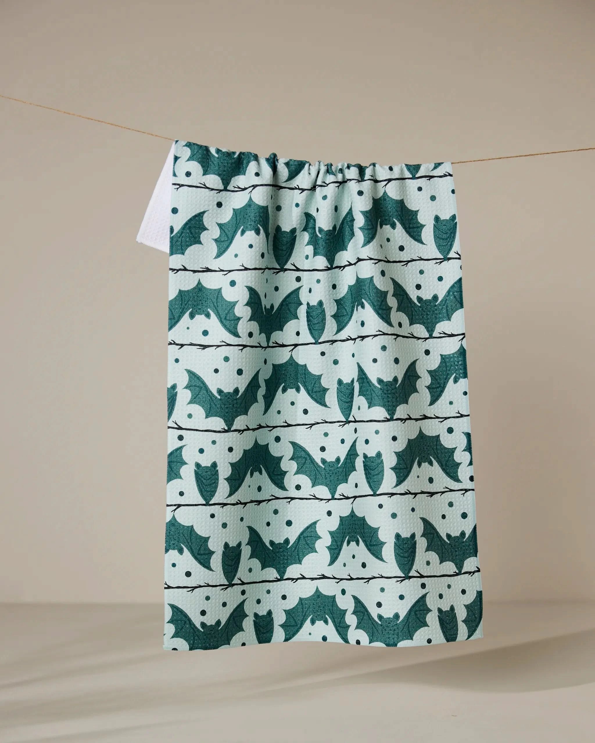 The Bats Stripes and Dots tea towel panel by Geometry, made from recycled materials, features a green and white pattern with stylized birds and abstract shapes, and hangs on a thin string against a neutral background.