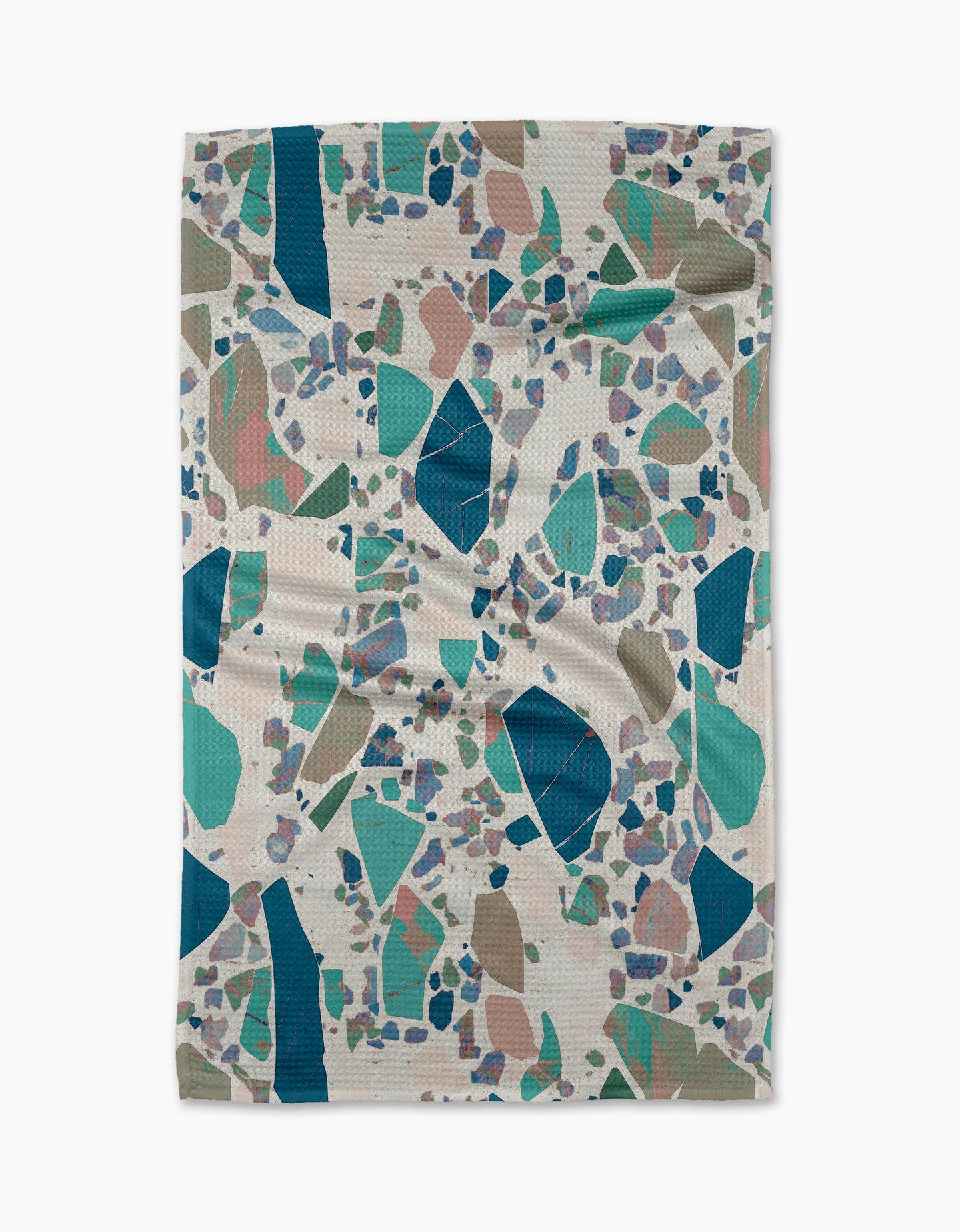 The Geometry Beryl tea towel is rectangular with a terrazzo pattern of scattered teal, green, blue, beige, and lavender shapes on a white background. The fabric has a lightly wrinkled, textured finish.