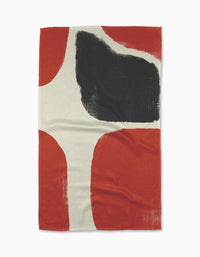 The Geometry Cast woven blanket features bold red, black, and off-white abstract shapes with painterly textures. Crafted from recycled materials, its irregular black form contrasts sharply with the surrounding red and cream tones.