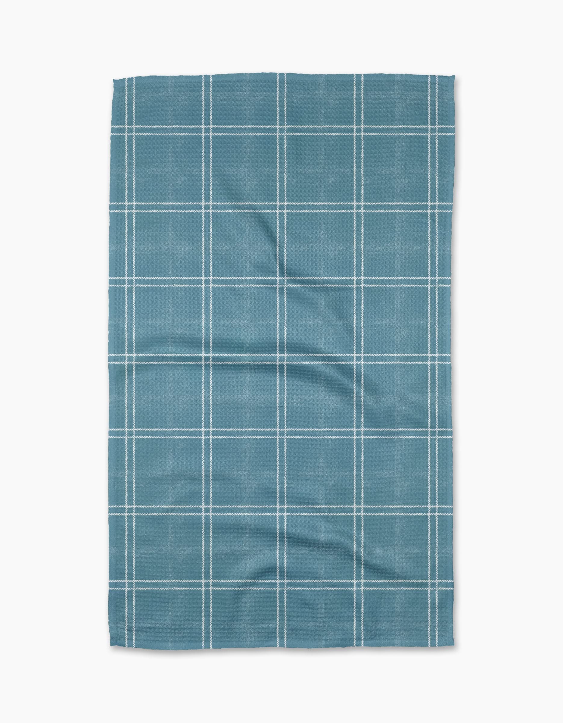 The Geometry Hearth Bay tea towel features a blue base with a white grid pattern. Ultra-absorbent and subtly wrinkled, this dish towel is shown laid flat against a white background.