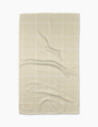 The Geometry Hearth Oat tea towel features a subtle white checkered pattern on beige recycled fabric, displayed flat with soft folds and creases against a white background.