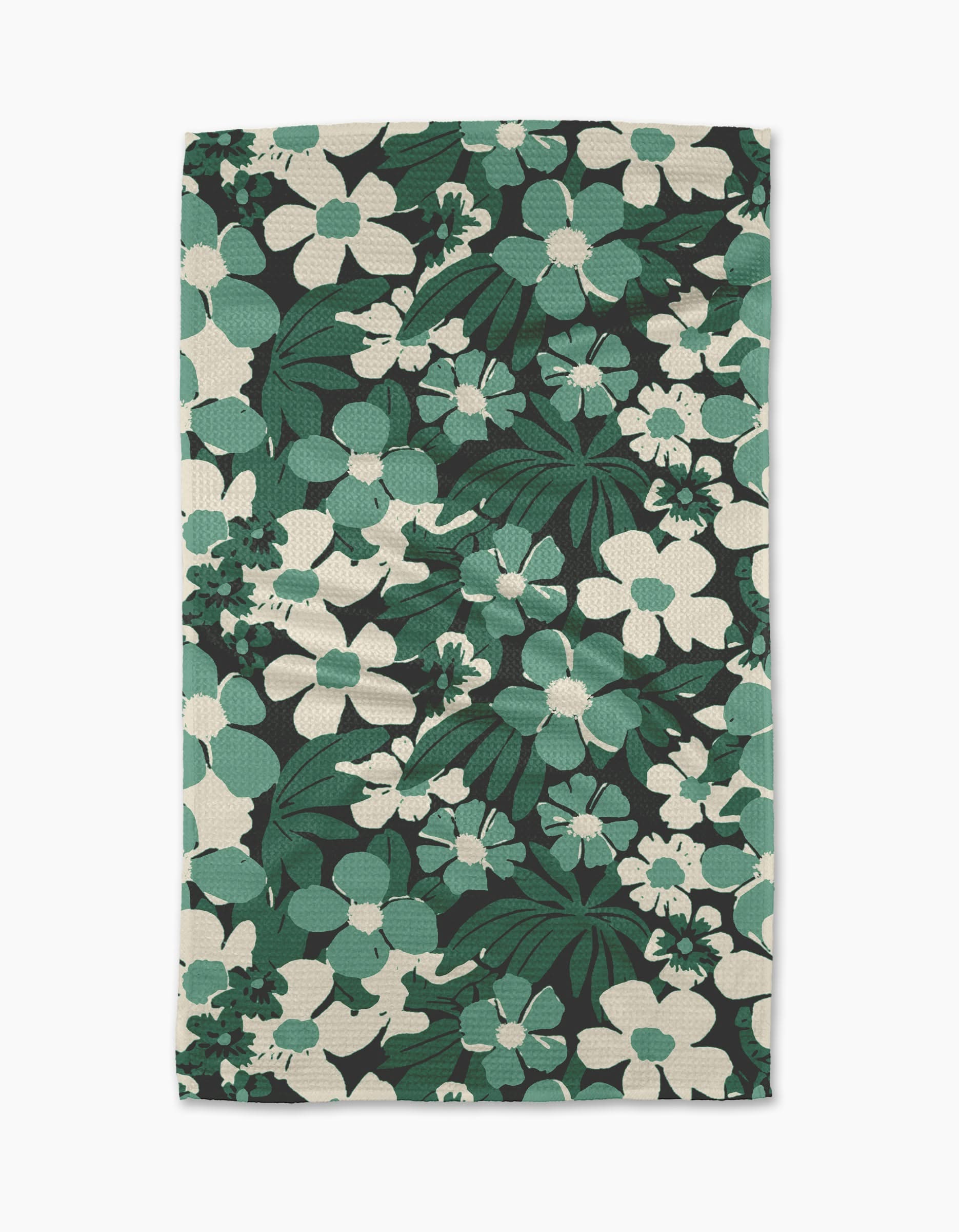 The Geometry Marlo Green tea towel features a bold floral design with large green and white flowers and leaves on a black background. Made from recycled materials, its fabric has a textured, woven look.