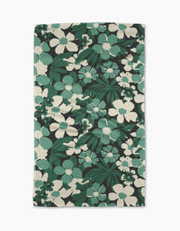 The Geometry Marlo Green tea towel features a bold floral design with large green and white flowers and leaves on a black background. Made from recycled materials, its fabric has a textured, woven look.