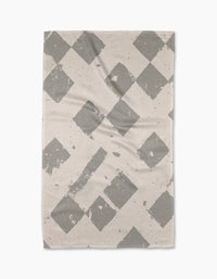 The Geometry Wisp Gray tea towel is rectangular and beige, featuring a gray diamond pattern with faded, distressed details, displayed flat on a white background.