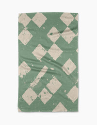 The Geometry Wisp Green tea towel features a textured green background with off-white, distressed diamond patterns. Made from recycled materials, its fabric has gentle creases and visible wear for a charming, lived-in look.