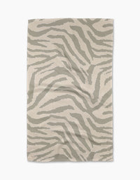 The Zira Gray tea towel by Geometry is a beige, rectangular cloth made from recycled materials, featuring a subtle abstract light gray zebra stripe pattern. The towel is shown laid flat on a white background.