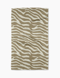 The Zira Tan tea towel by Geometry features a white zebra stripe pattern on rectangular beige fabric, displayed flat on a white background.