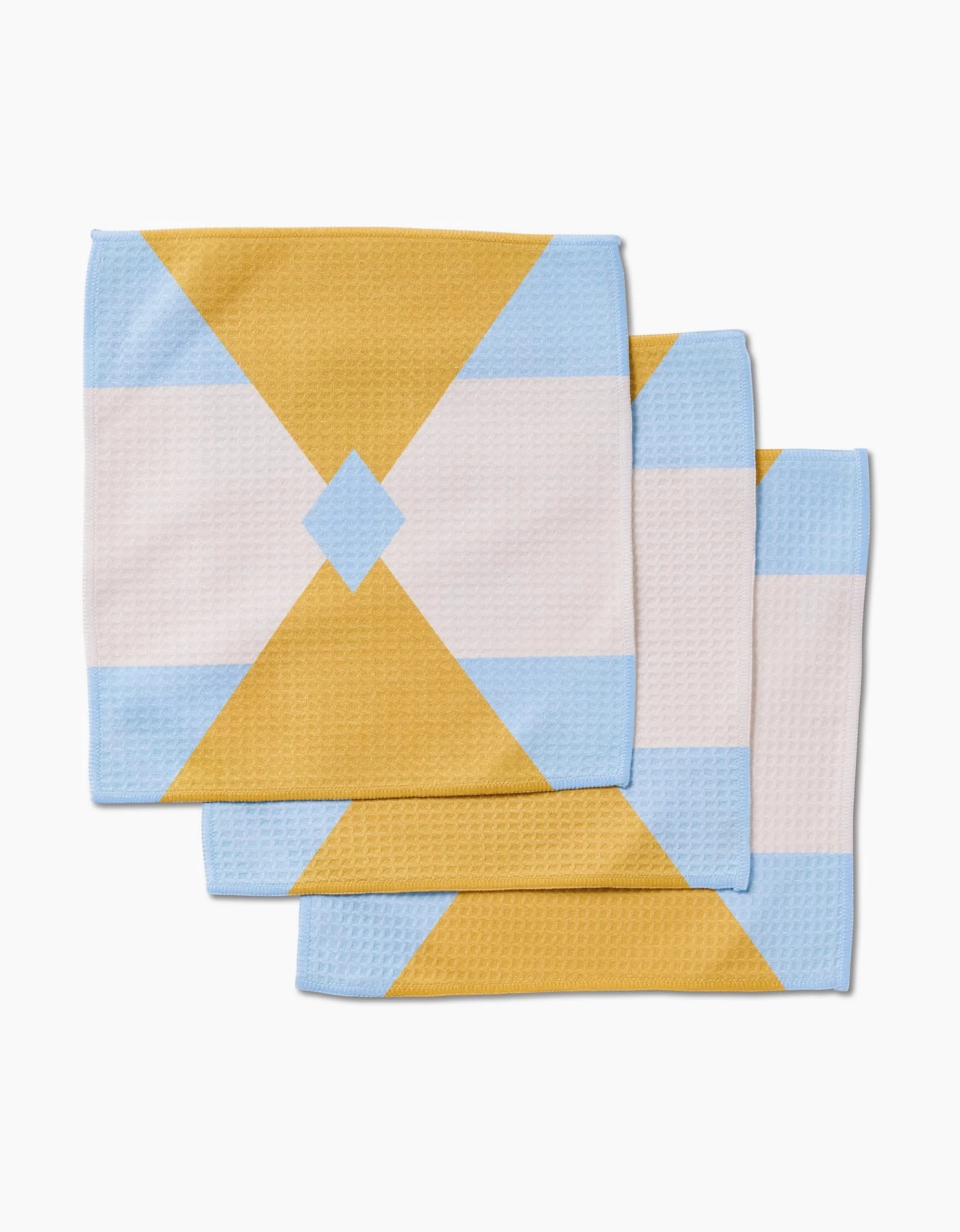 Three folded GEOMETRY Balanced Blue ultra-absorbent washcloths featuring a geometric pattern with intersecting triangles and a central diamond in yellow, light blue, and white, displayed on a white background.