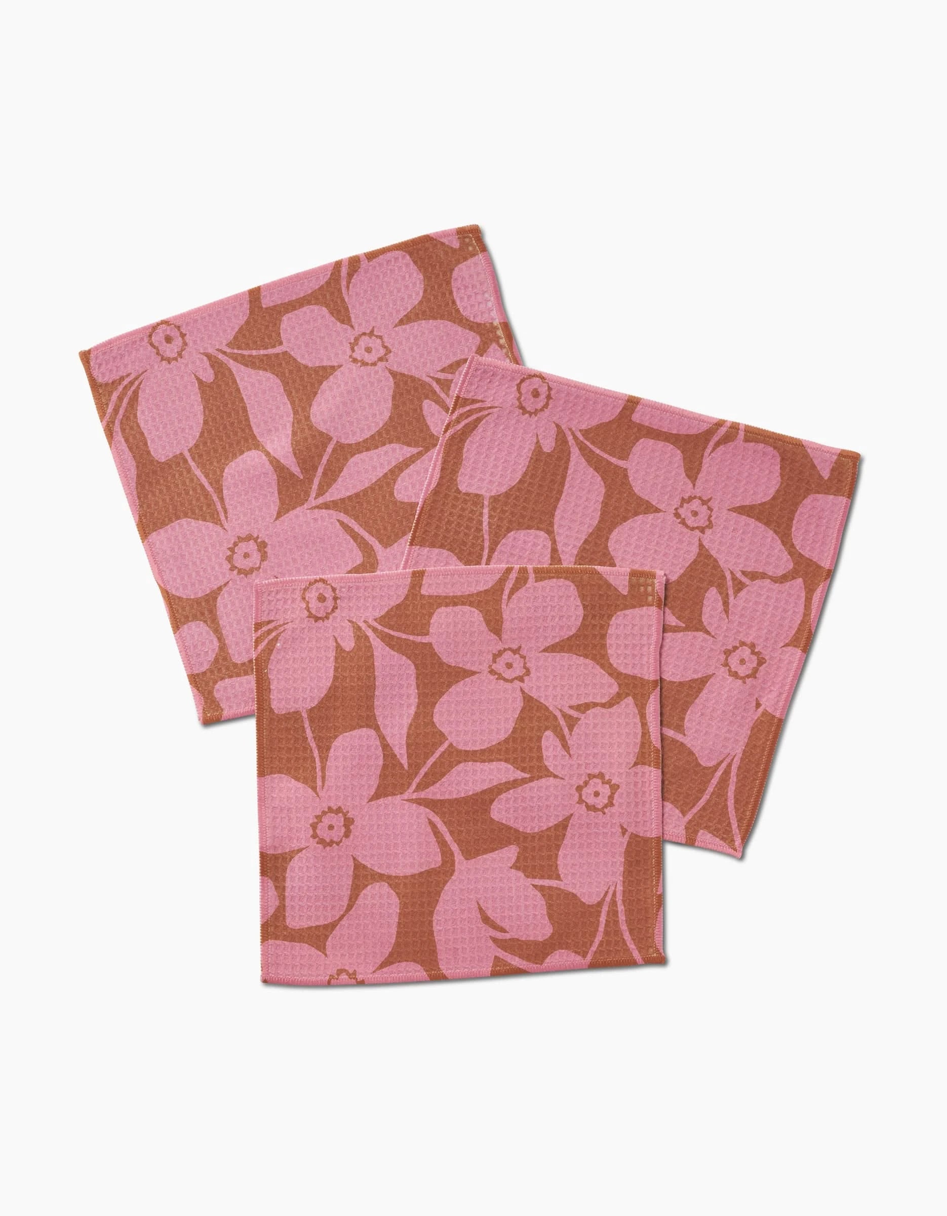 Three reusable GEOMETRY Luxe Washcloths in the Big Fuchsia Flowers design, featuring a pink floral pattern on brown, are slightly overlapped on a white surface. Made with ultra-absorbent Geoweave technology for effective cleaning.