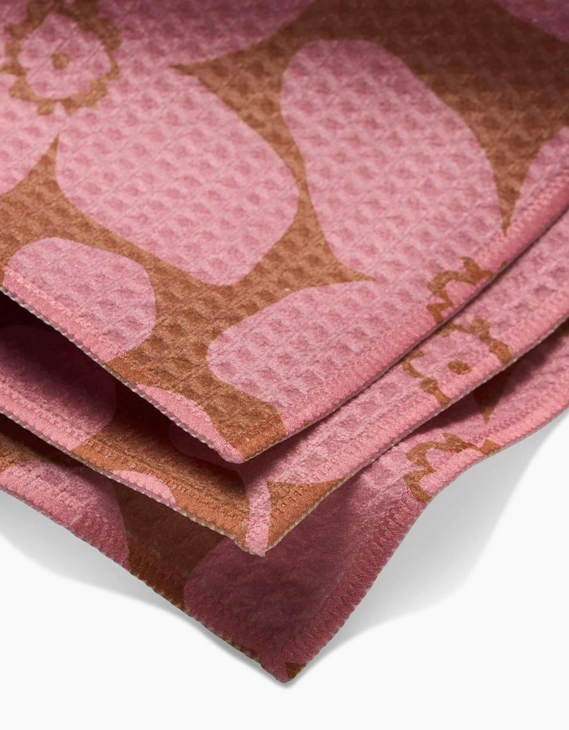 A close-up of folded, textured pink fabric with a brown floral pattern and waffle weave highlights the ultra-absorbent Big Fuchsia Flowers washcloth by GEOMETRY, crafted with Geoweave technology for superior softness and function.