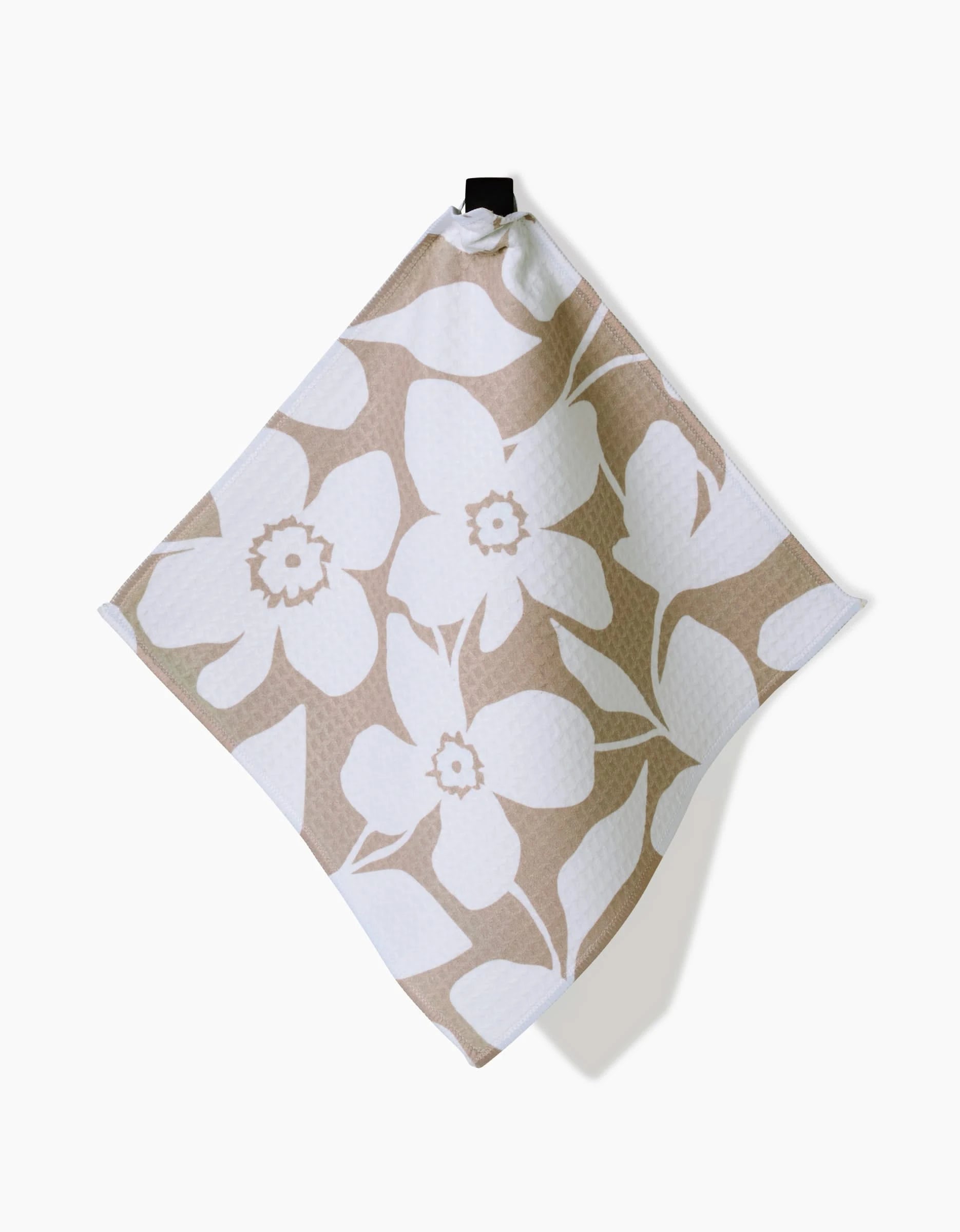 The GEOMETRY Big Tan Flowers kitchen towel, featuring a large beige and white floral design and ultra-absorbent Geoweave technology, hangs from a black loop against a white background.