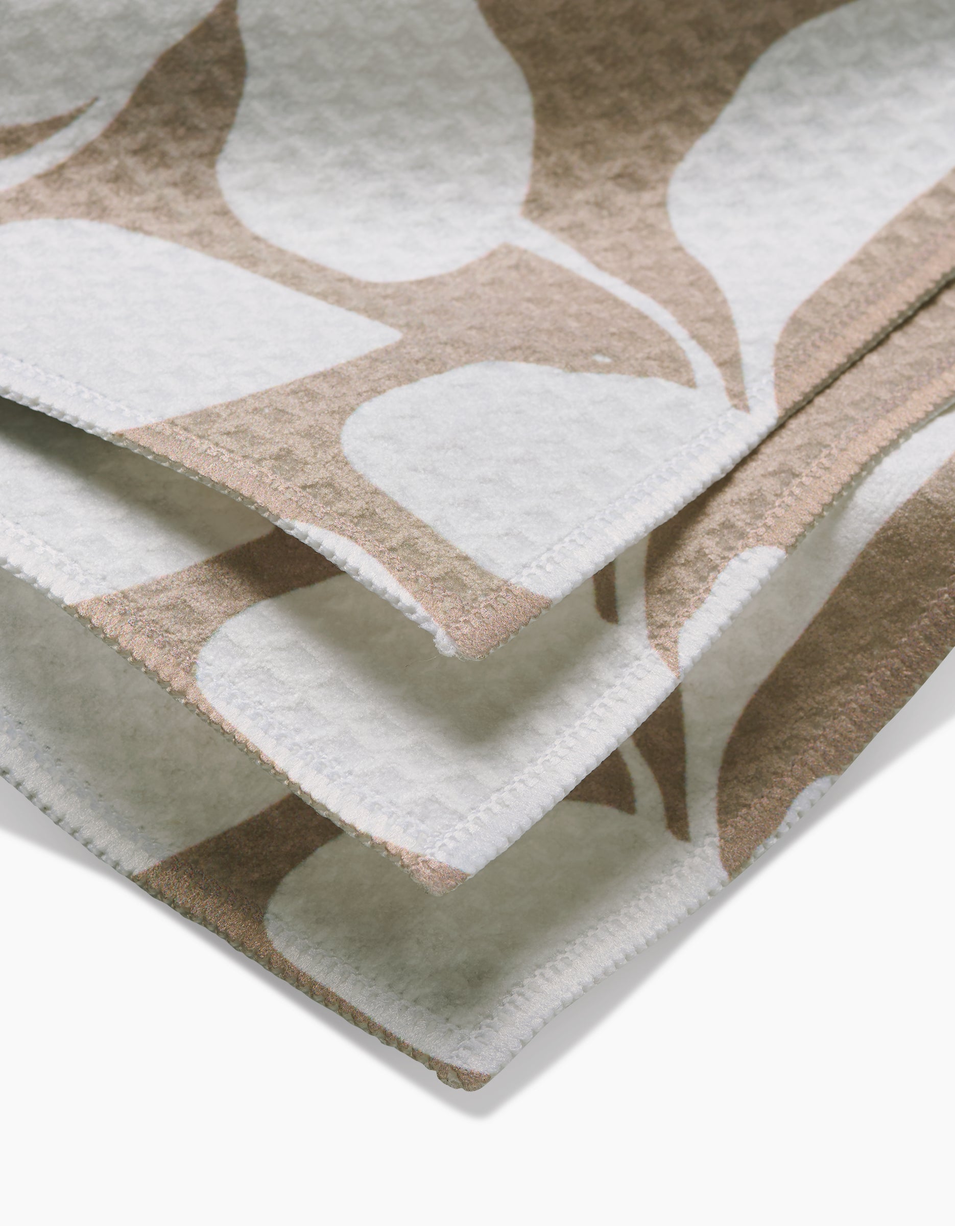 Close-up of Big Tan Flowers by GEOMETRY—a beige and white fabric with a leaf-like pattern and textured waffle weave, neatly finished edges, and layering, crafted with Geoweave technology for ultra-absorbent Luxe Washcloths.