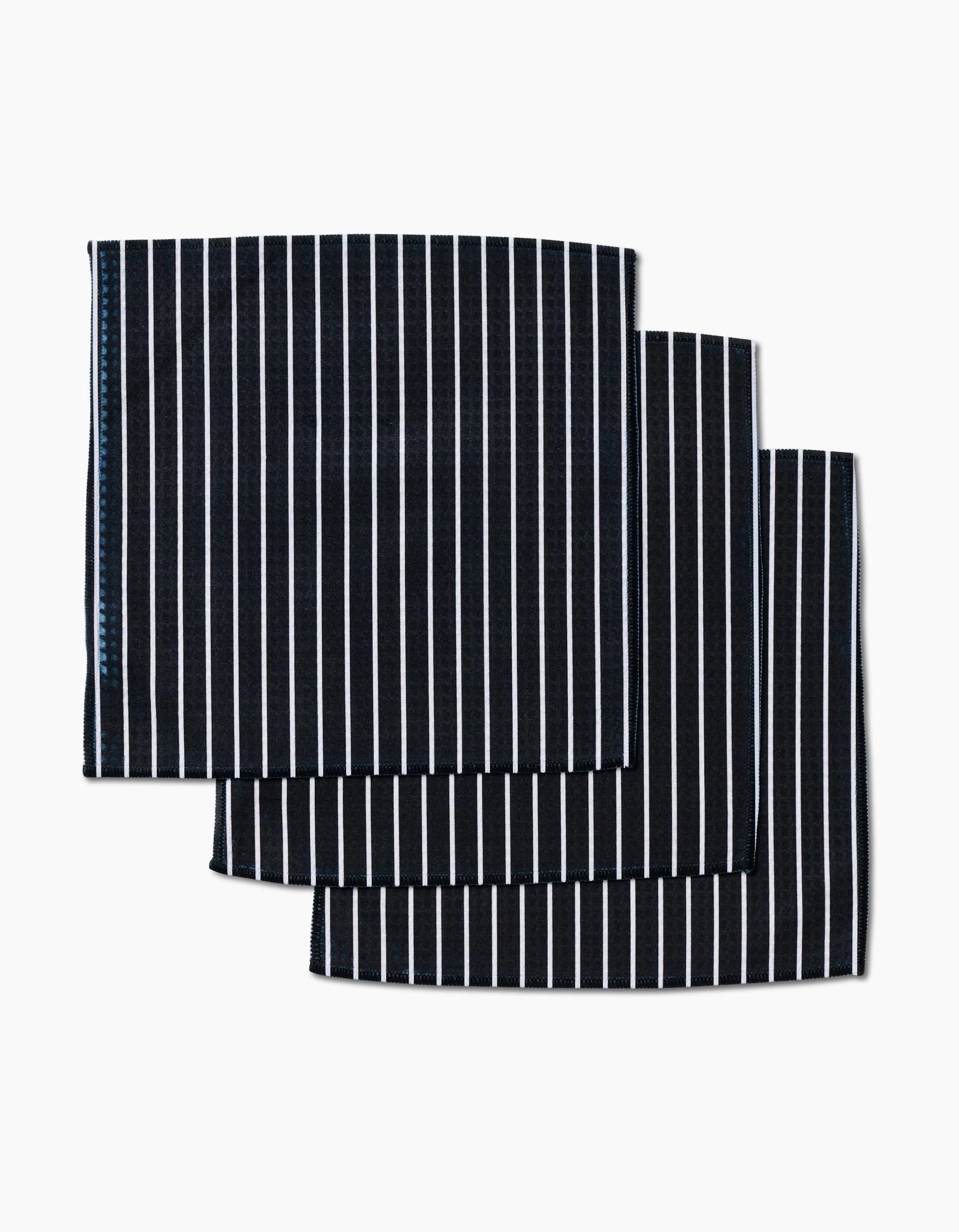 Three neatly folded Black Linen napkins by GEOMETRY, featuring a sleek black hue and refined design, are stacked with a slight offset against a white background to highlight their ultra-absorbent quality and understated elegance.
