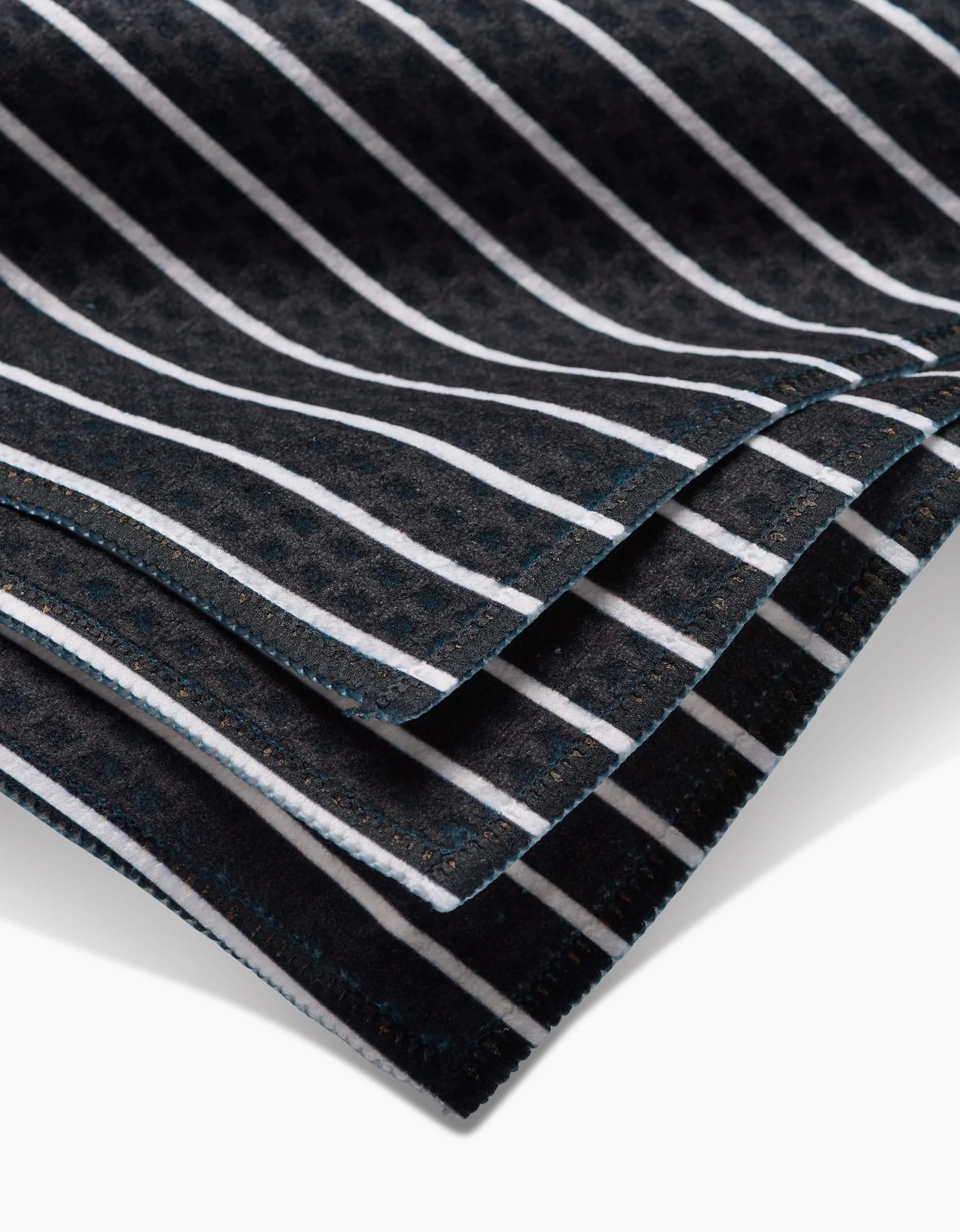 A close-up photo of folded Black Linen by GEOMETRY, showing evenly spaced vertical white stripes and neatly stitched edges, crafted with Geoweave technology for ultra-absorbent Luxe Washcloths.