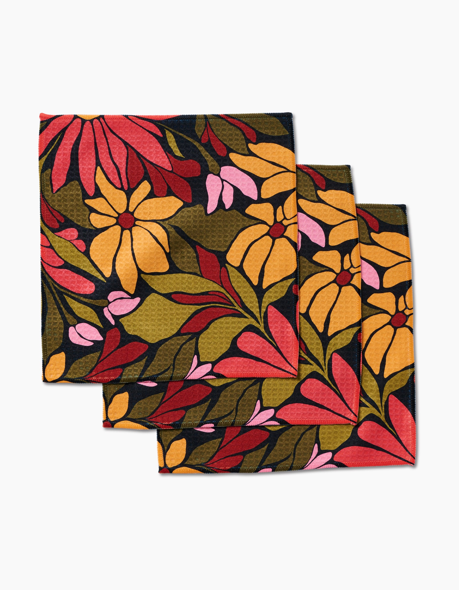 Three stacked GEOMETRY Luxe Washcloths in the Blooming Black pattern, featuring bold pink, yellow, and red flowers with green leaves on a dark background, crafted with ultra-absorbent Geoweave technology.