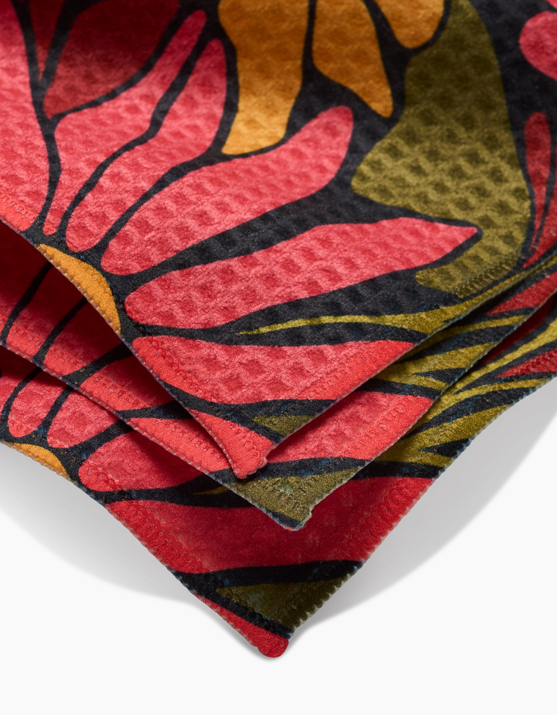 Close-up of GEOMETRYs Blooming Black washcloths, showcasing ultra-absorbent fabric with a vibrant abstract floral pattern in red, yellow, green, and black and textured, overlapping edges.
